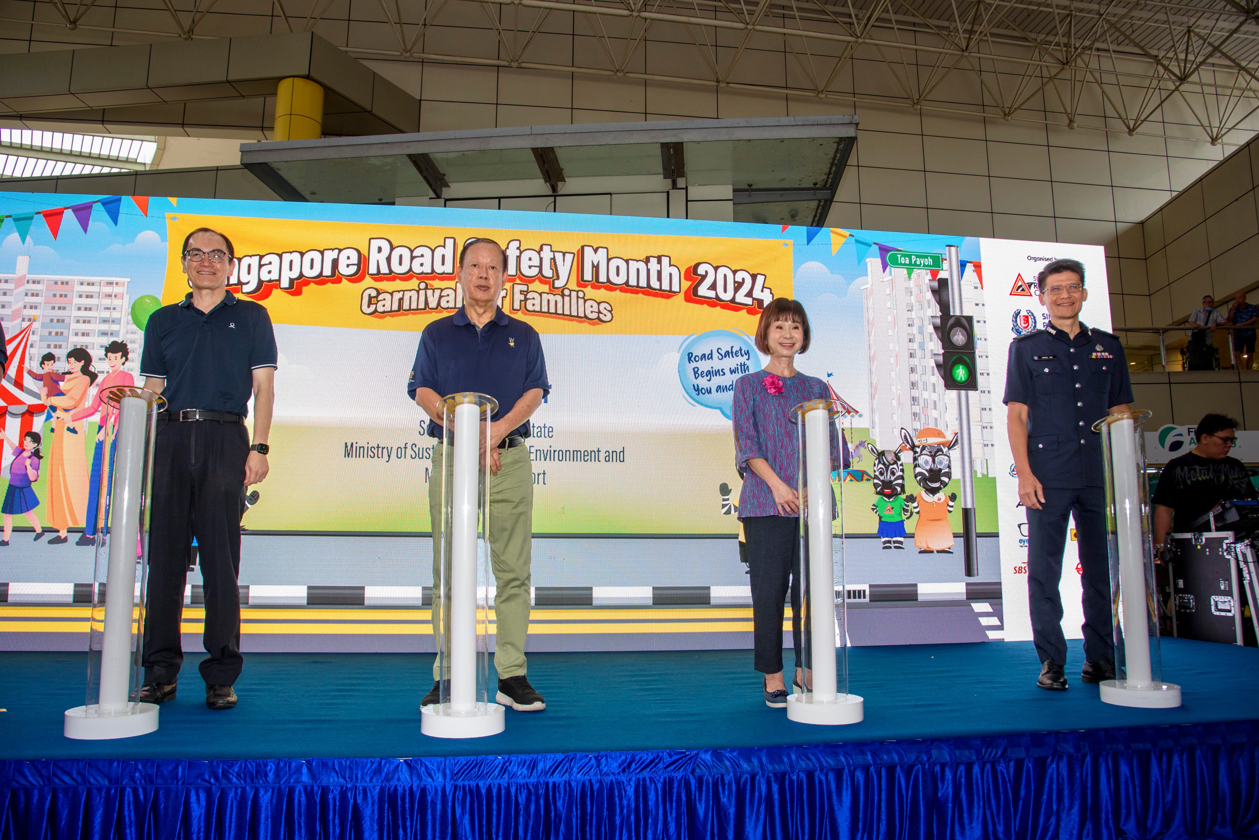 Four individuals on stage with a colorful backdrop for "Singapore Road Safety Month 2024 Carnival for Families".