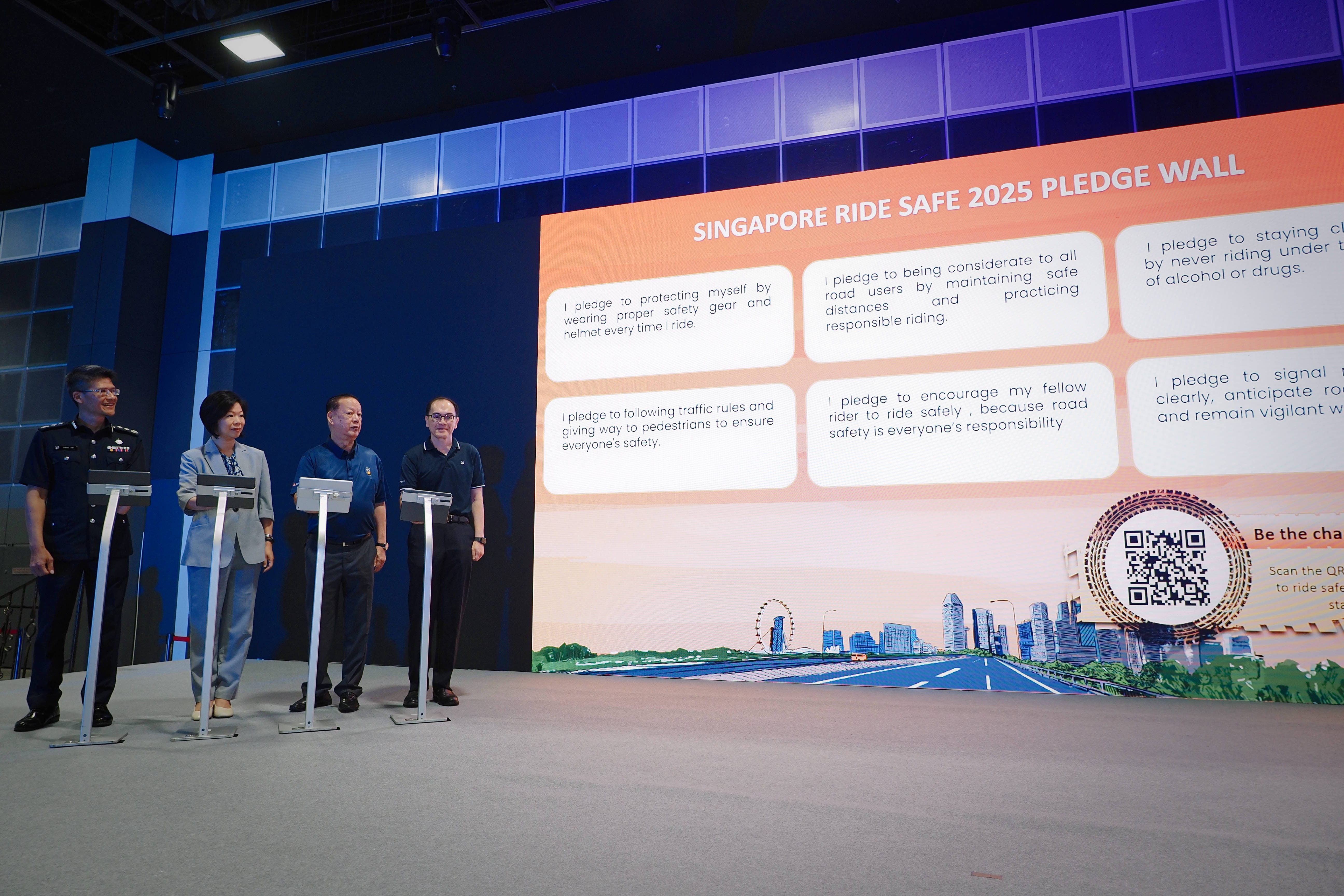 A pledge wall displaying safety pledges for riders, with four individuals standing in front of podiums.