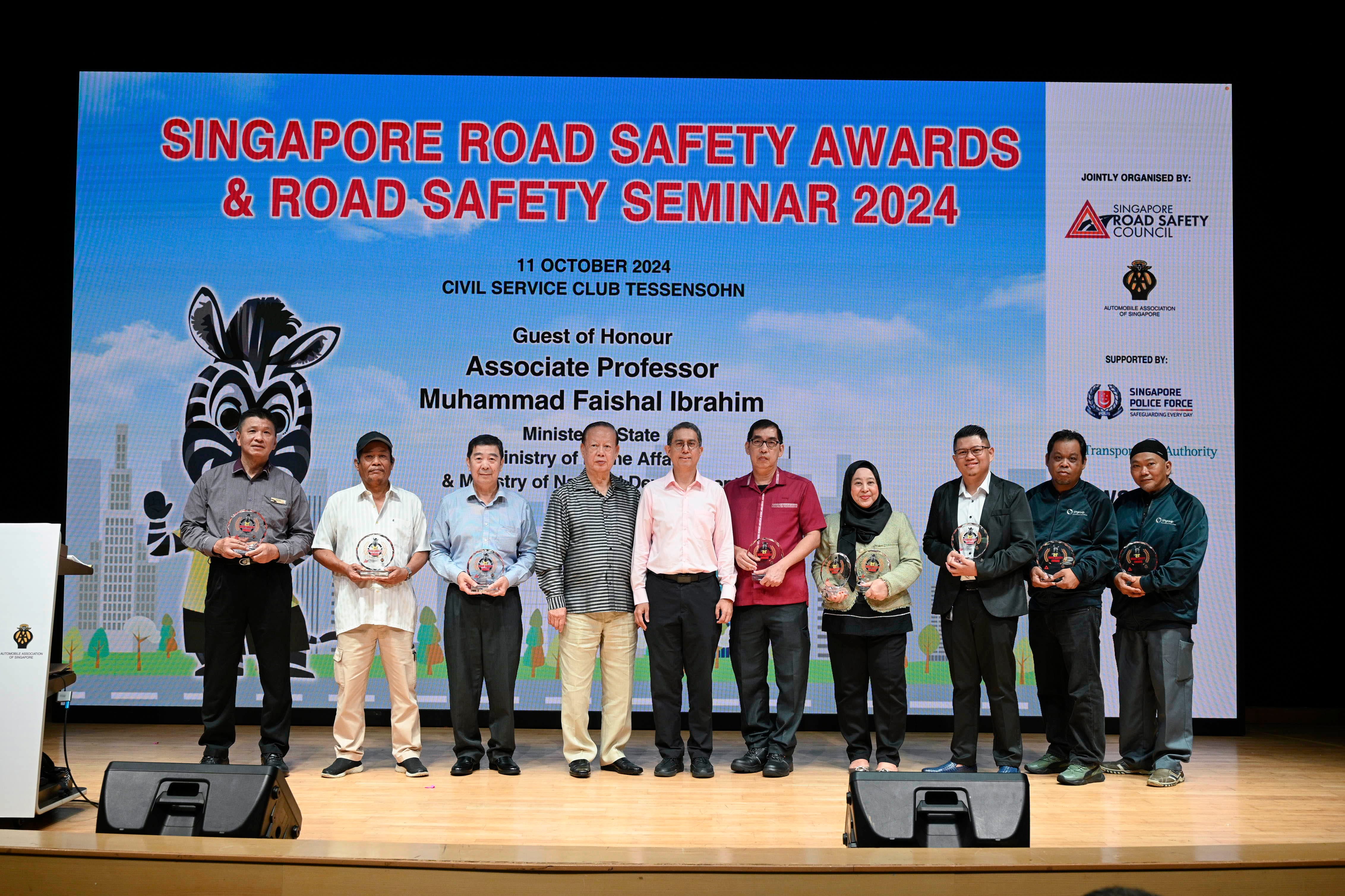 Eight people on stage holding awards, standing before a screen with "Singapore Road Safety Awards & Road Safety Seminar 2024."