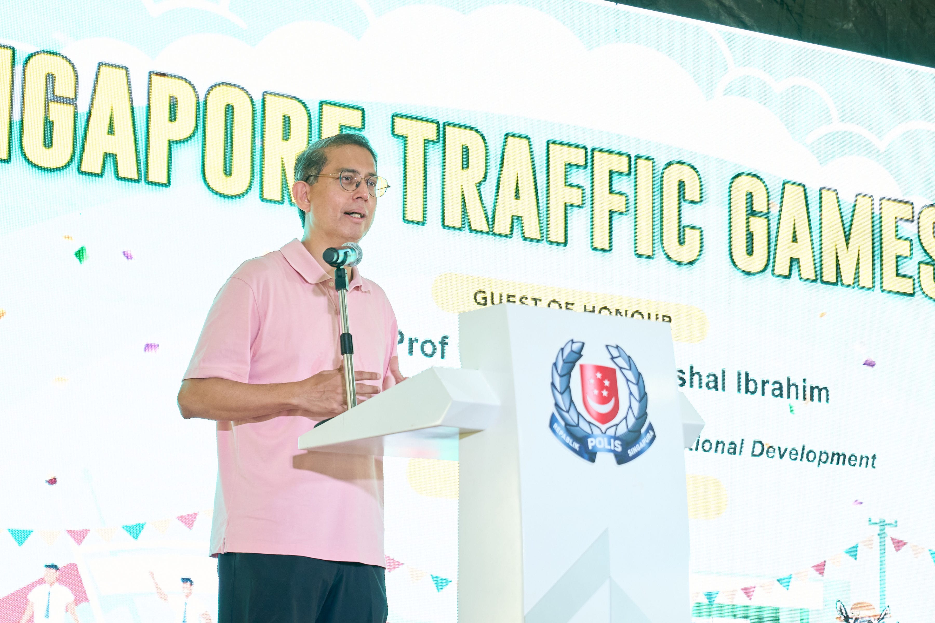 Man in pink shirt speaks at podium labeled "Polis"; background says "Singapore Traffic Games."