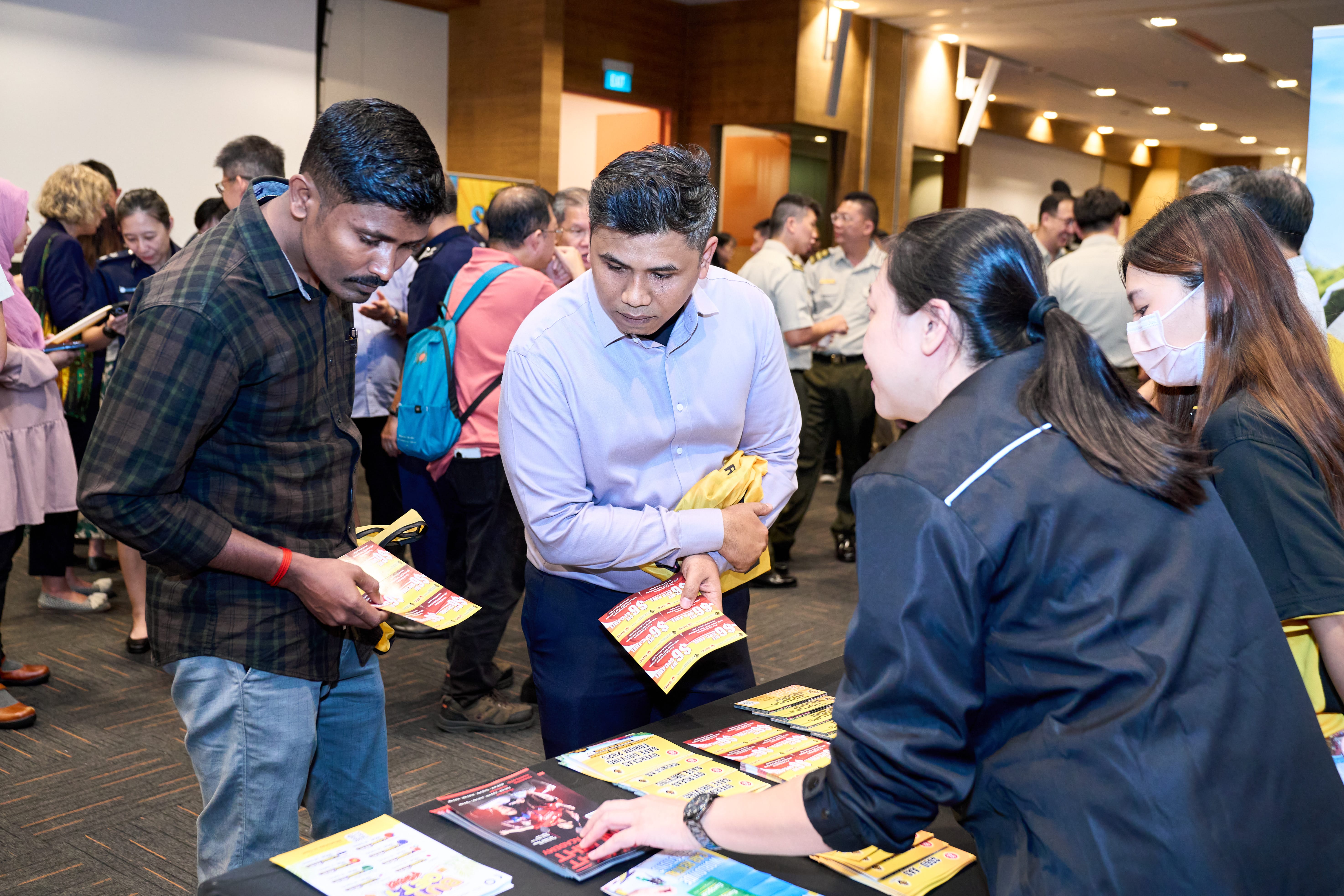 People looking at pamphlets on a table at an event with others conversing in the background.