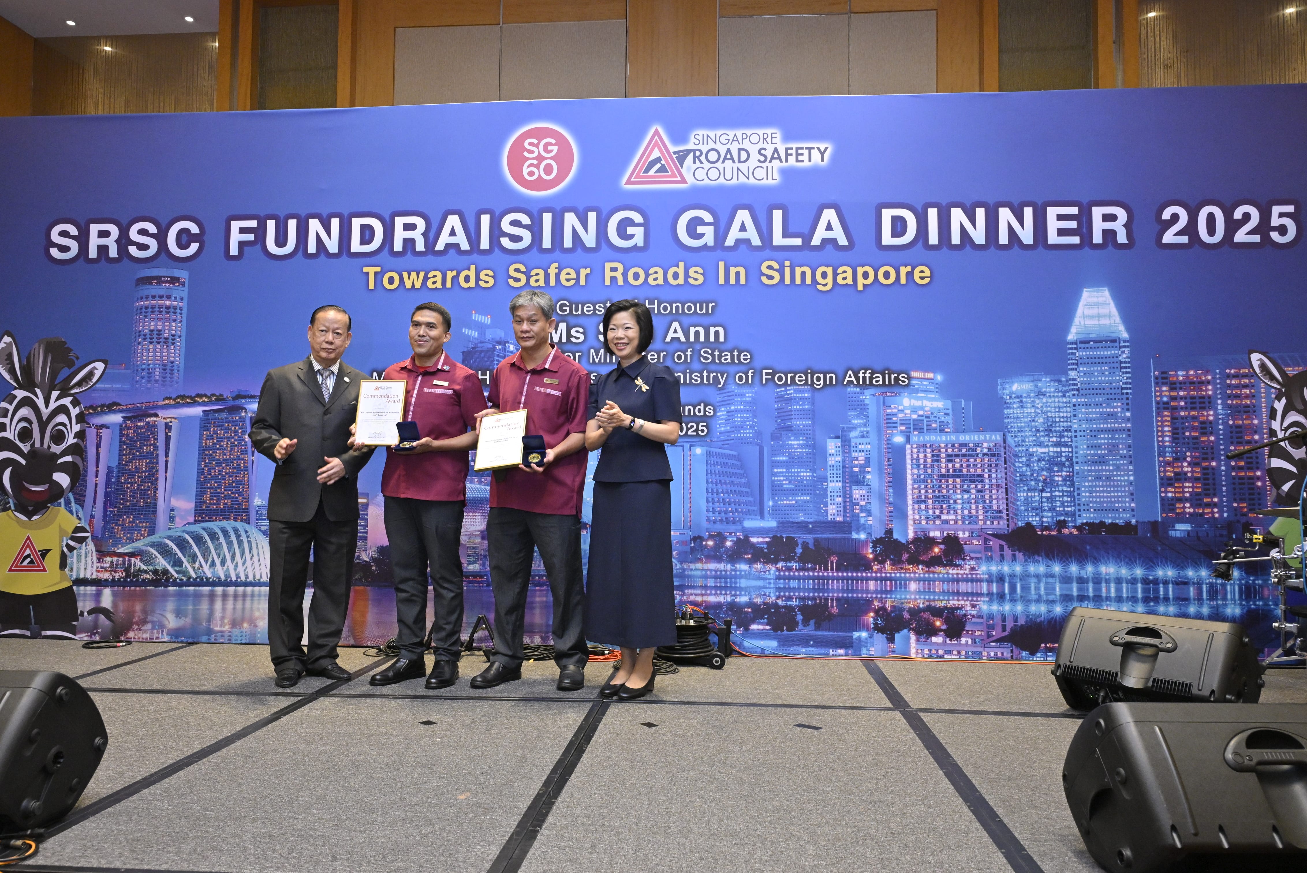 Four individuals on stage during a fundraising gala, with a cityscape and event details in the backdrop.