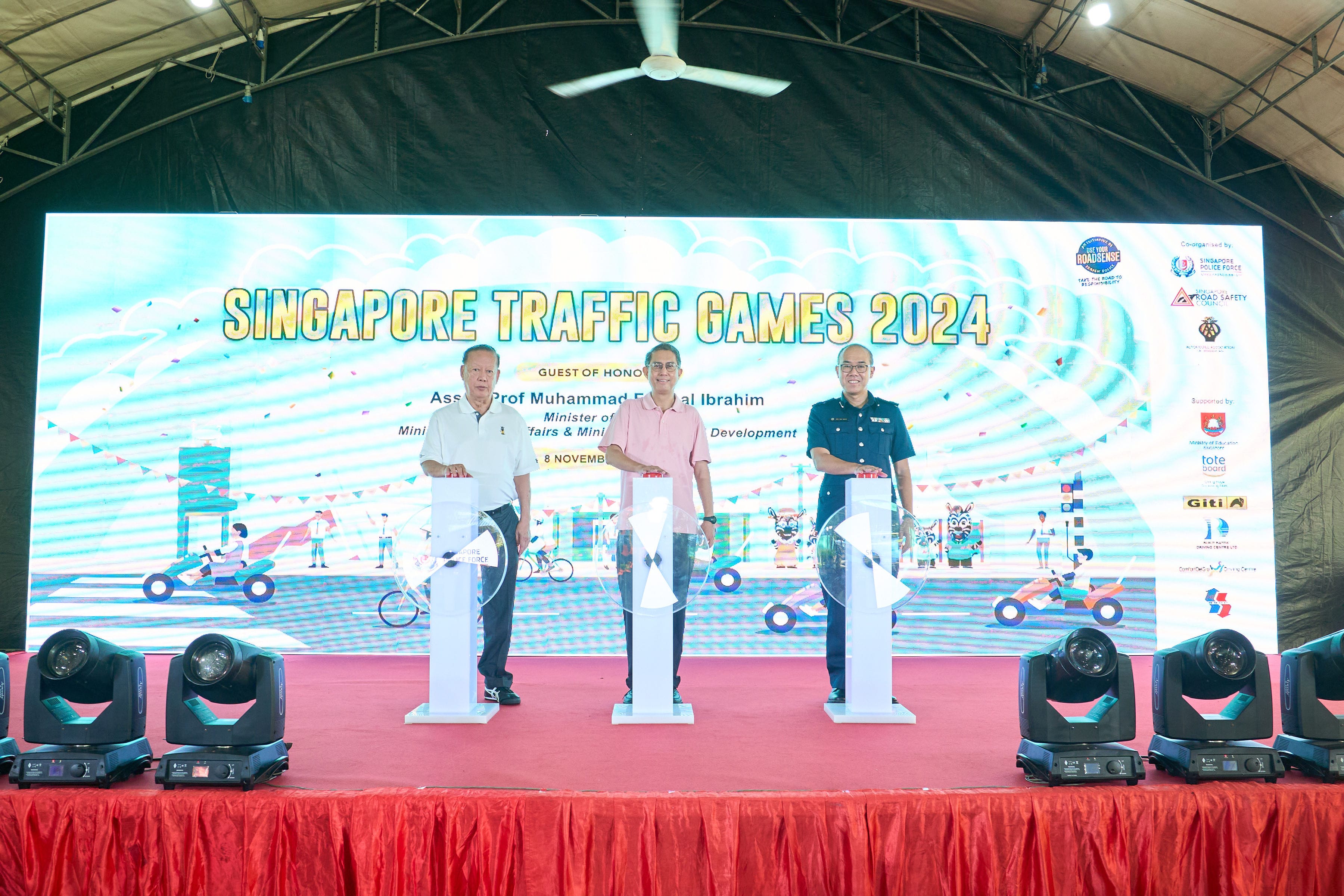Three people stand on stage in front of a screen reading "Singapore Traffic Games 2024" in large letters.