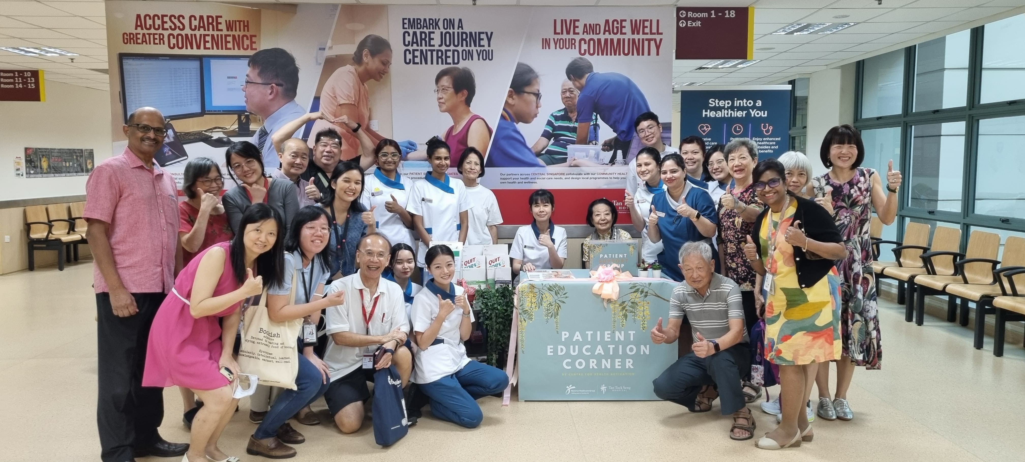 Group of people posing in front of posters promoting healthcare services at a patient education corner in a hospital.