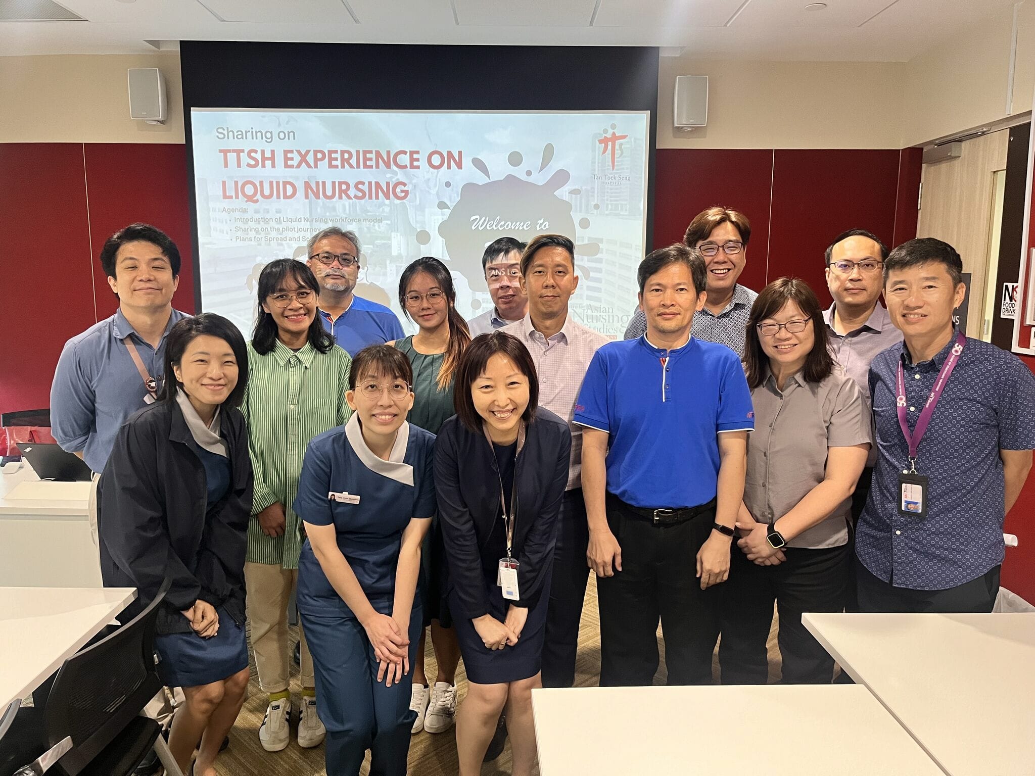 A group of people stand indoors with a presentation slide in the background titled "Sharing on TTSH Experience on Liquid Nursing."