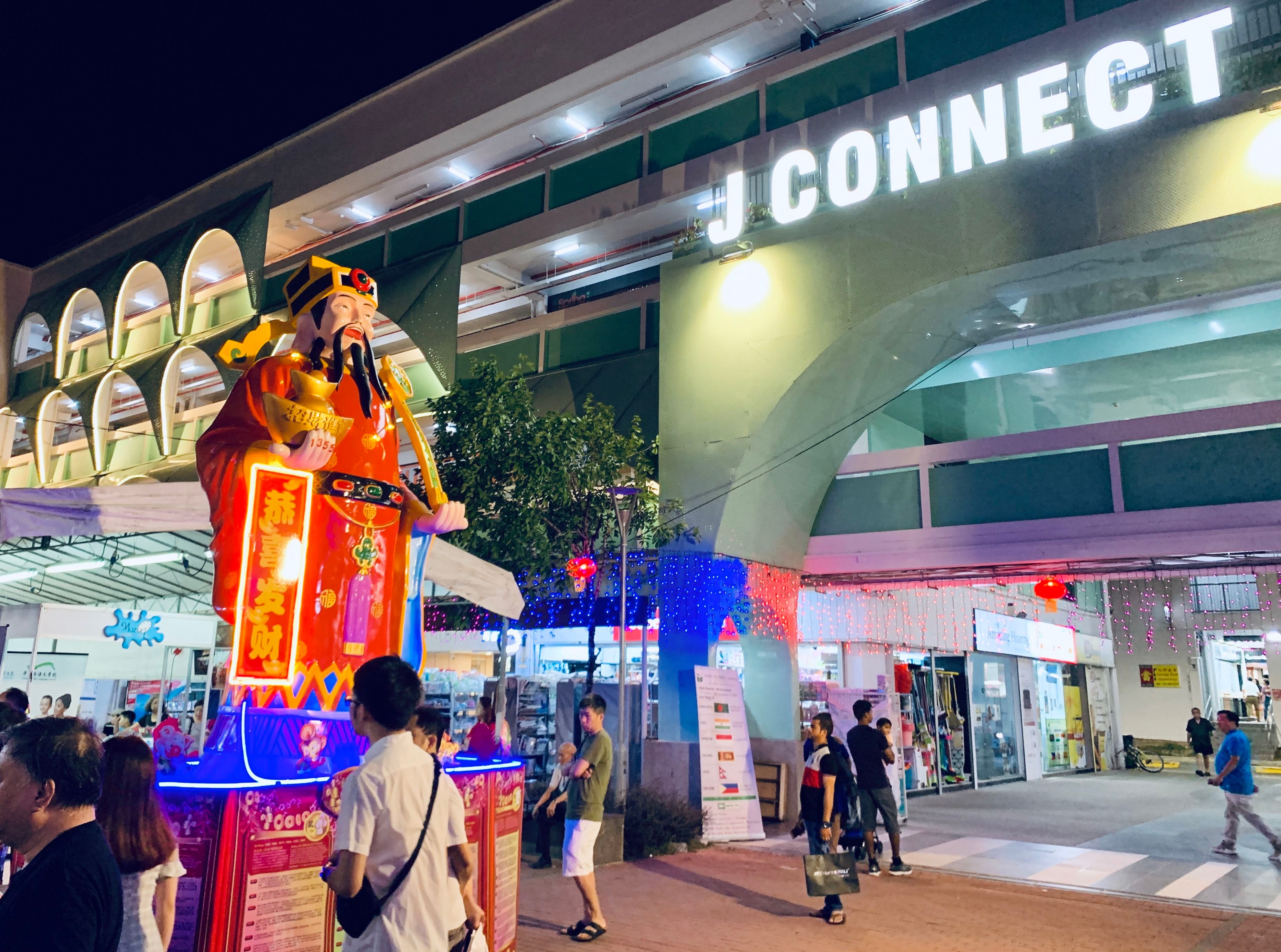 People gather around a colorful statue in front of a building labeled "J CONNECT" at night.