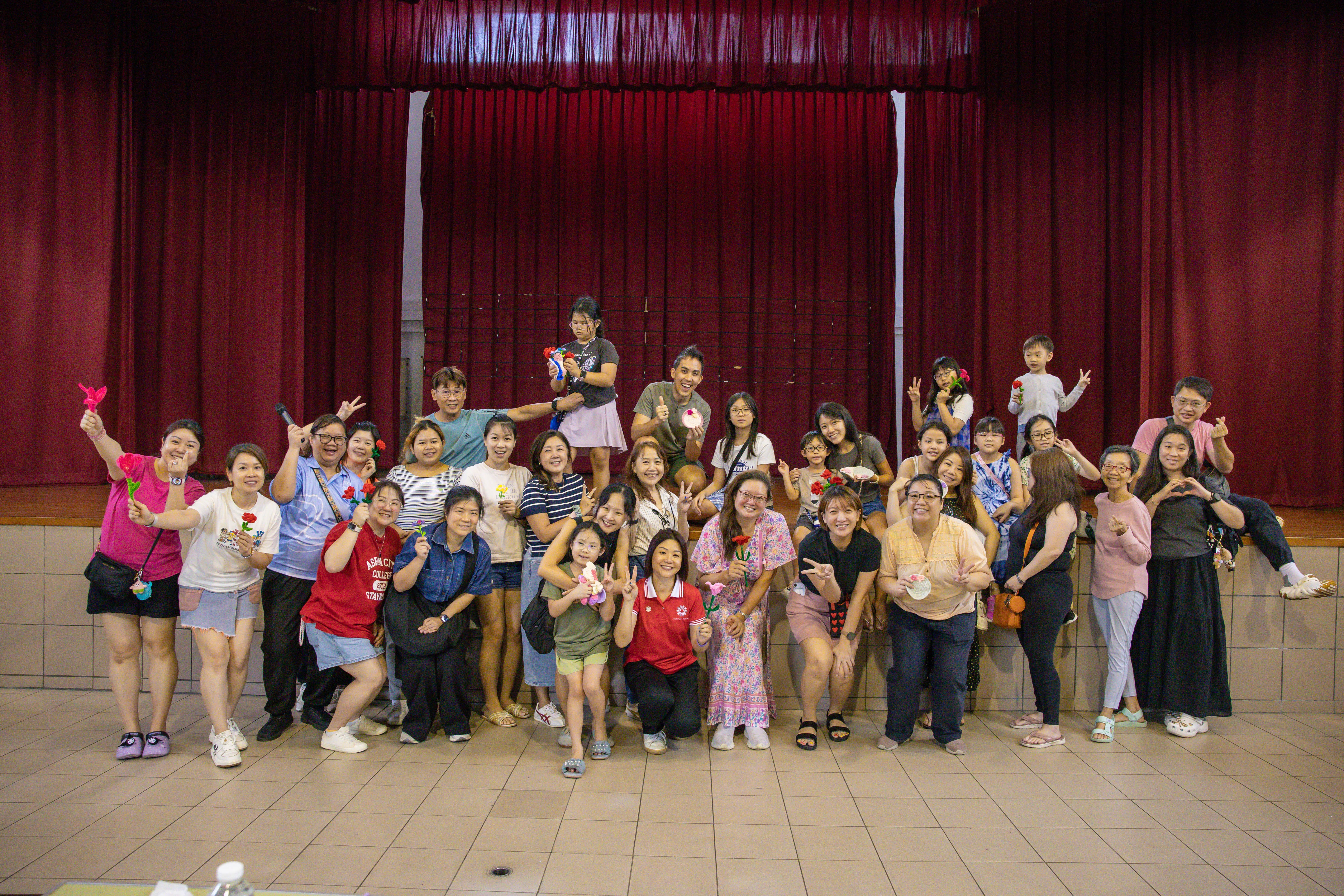 Participants pose on stage with handmade flowers after a craft activity.