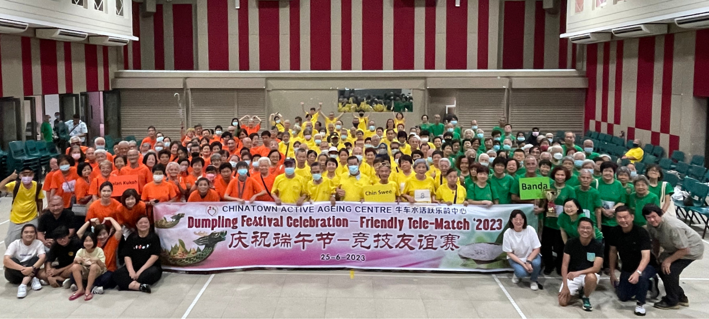 Participants from multiple teams pose behind a tele-match event banner in a hall.