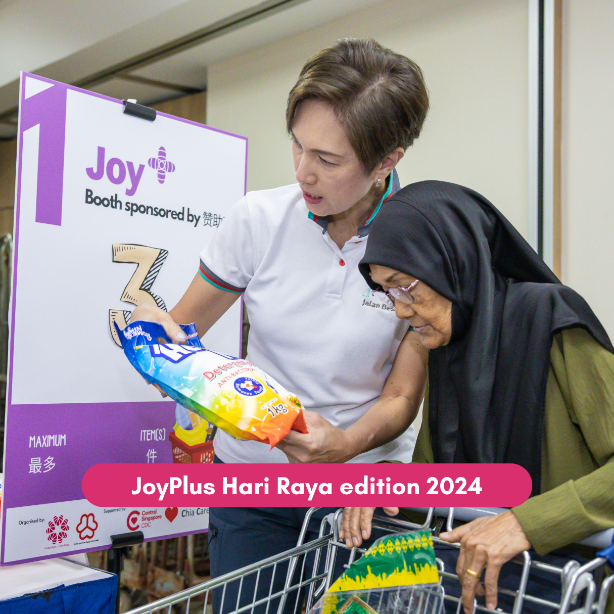 Volunteer helps senior choose groceries at JoyPlus Hari Raya event.
