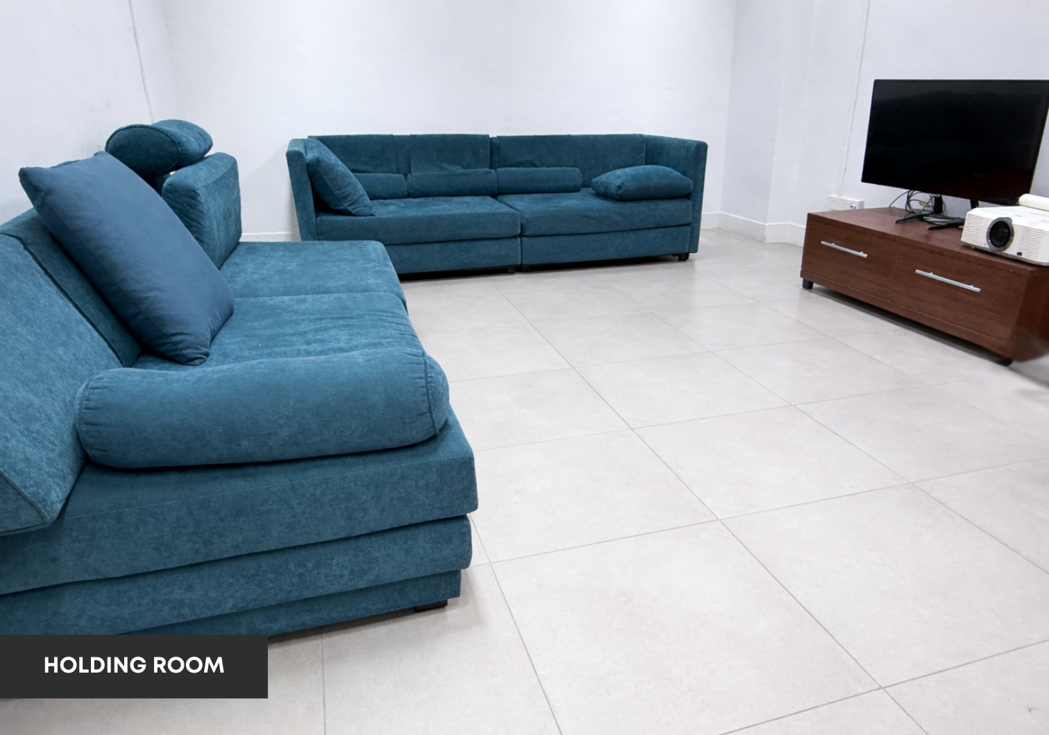 Holding room with blue sofas, television and projector.