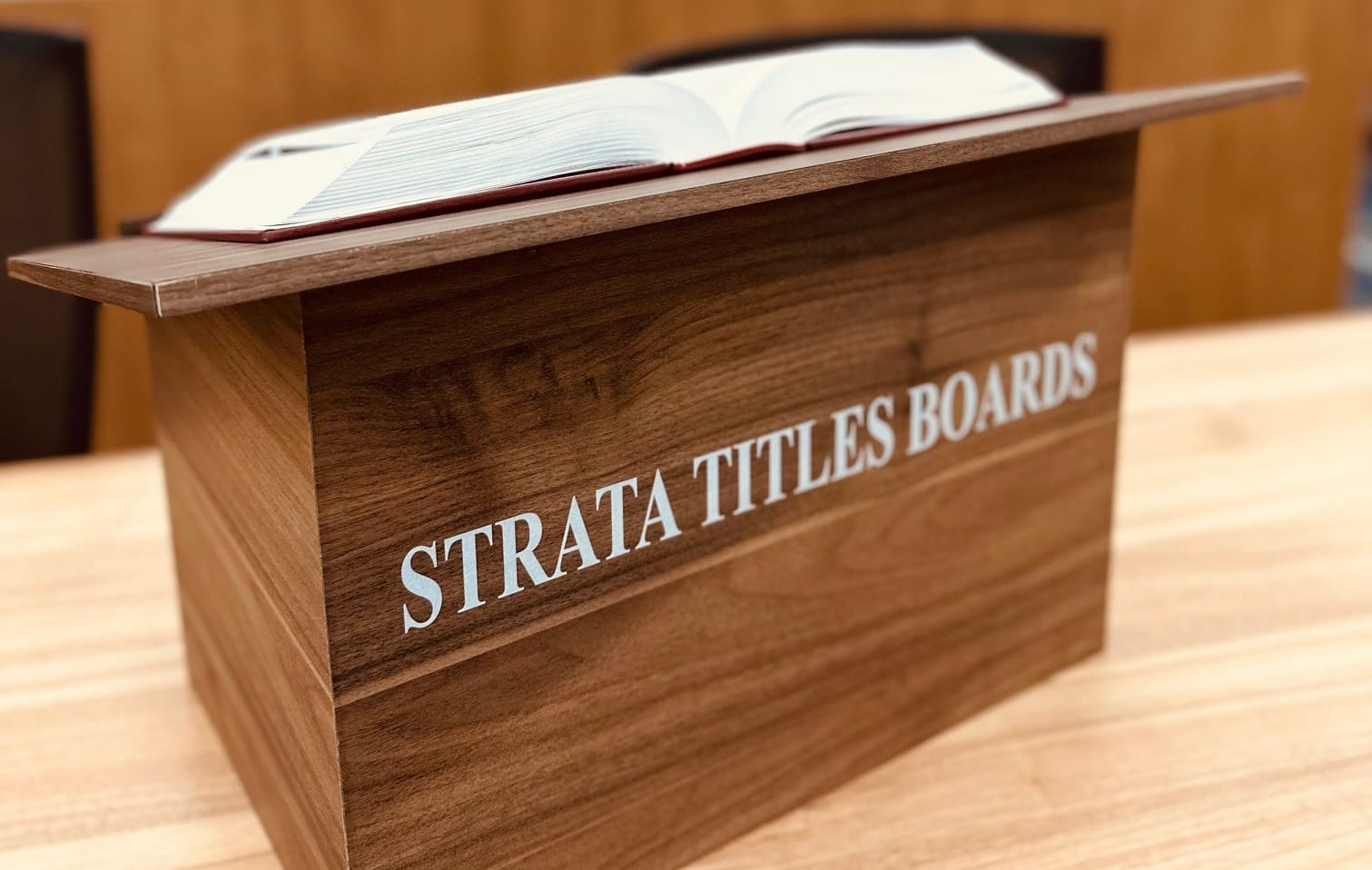 A wooden lectern with "STRATA TITLES BOARDS" inscribed on it and an open book placed on top.
