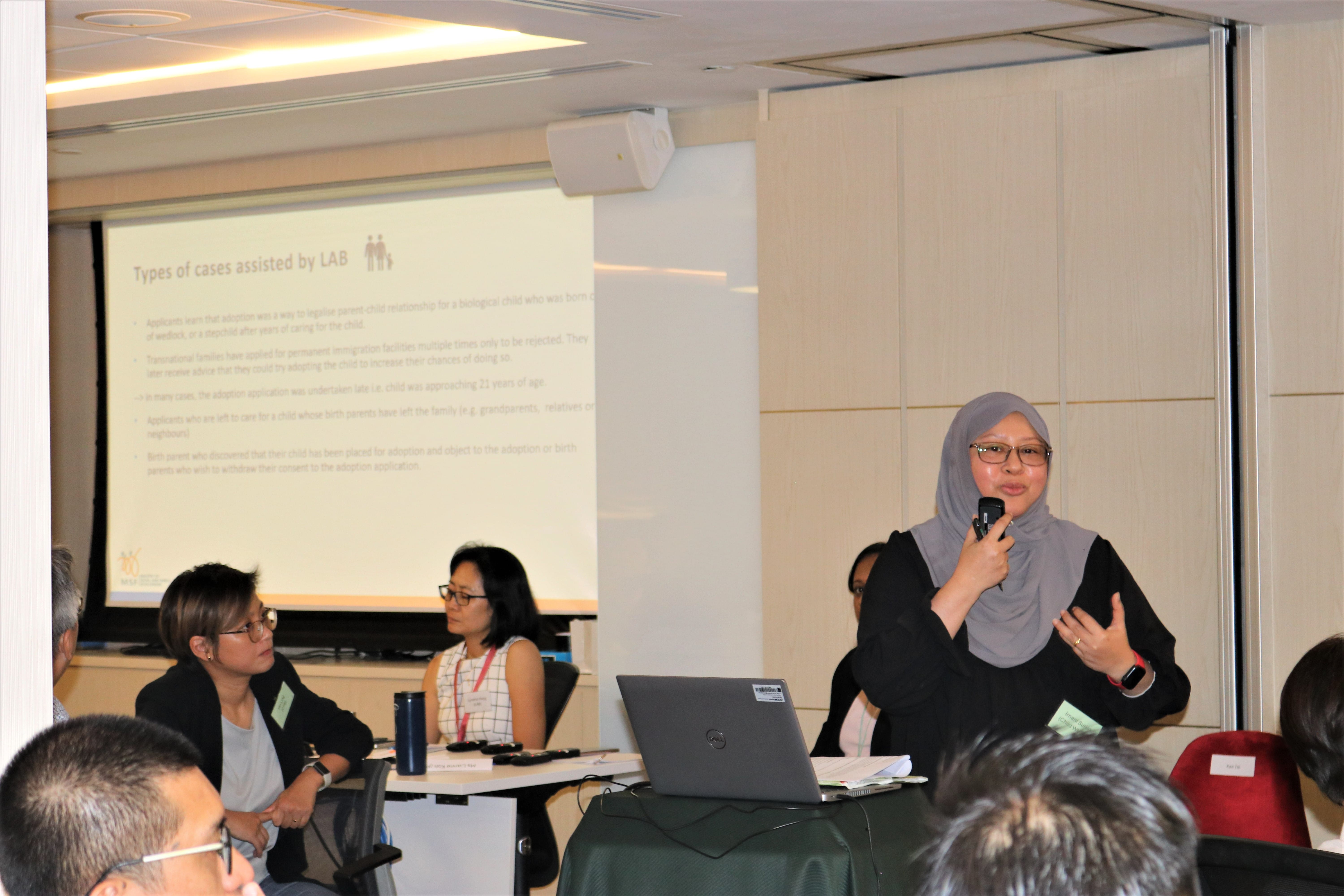 A woman in a gray hijab speaks into a microphone at a seminar, with a projected slide titled "Types of cases assisted by LAB."