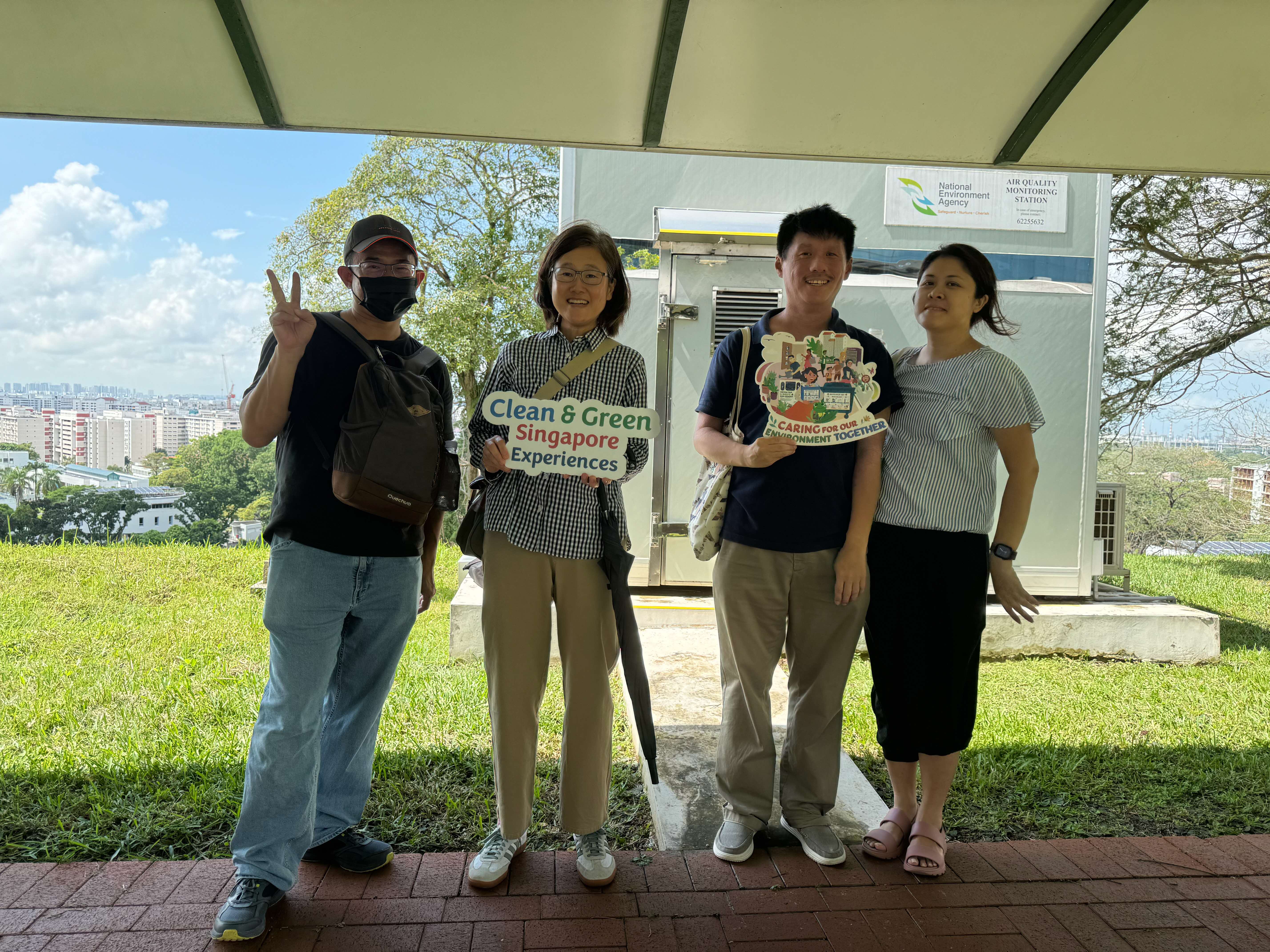 Four smiling people pose outdoors holding Clean & Green Singapore signs.