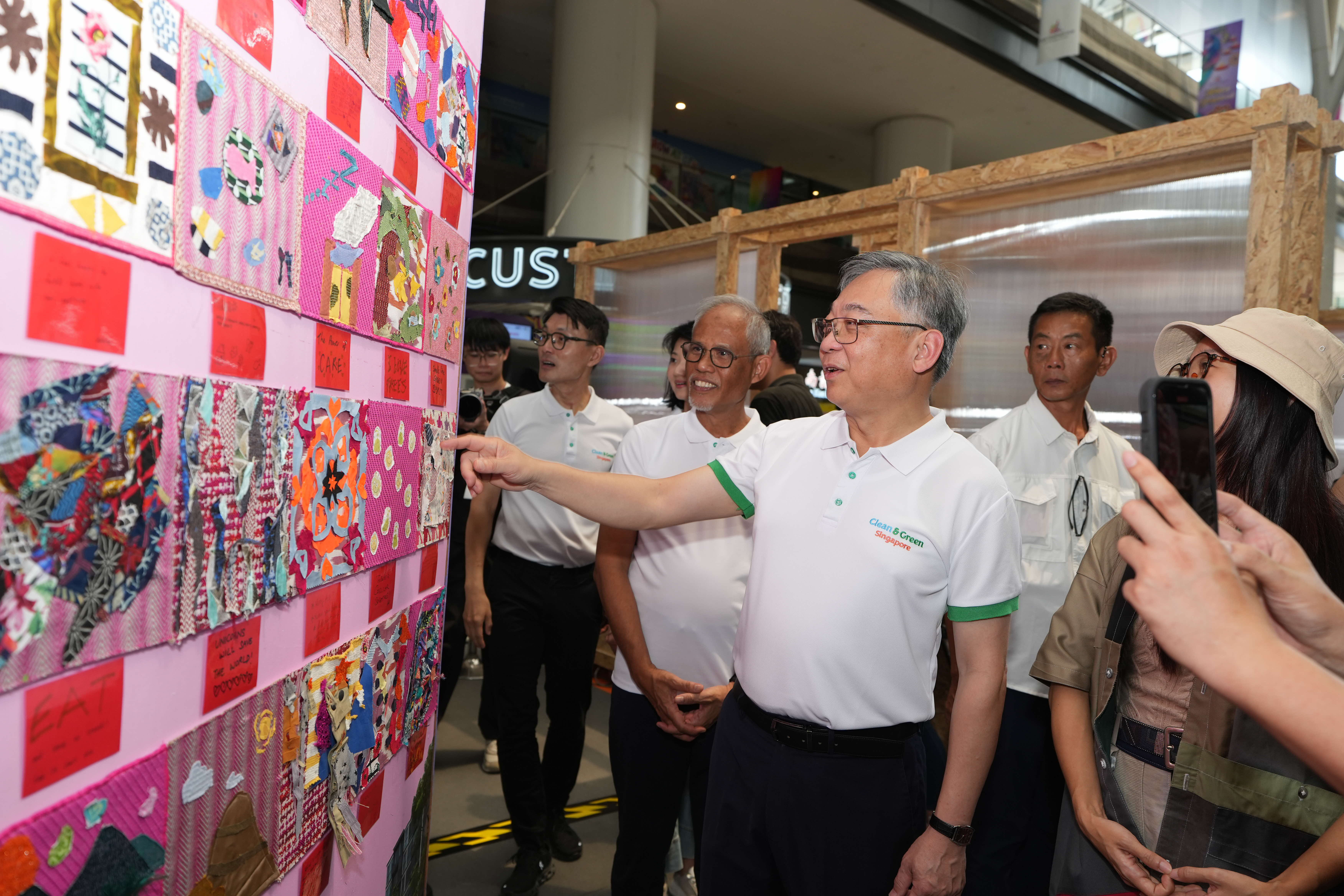 DPM Gan in a Clean & Green Singapore shirt points at a colourful fabric patchwork display.