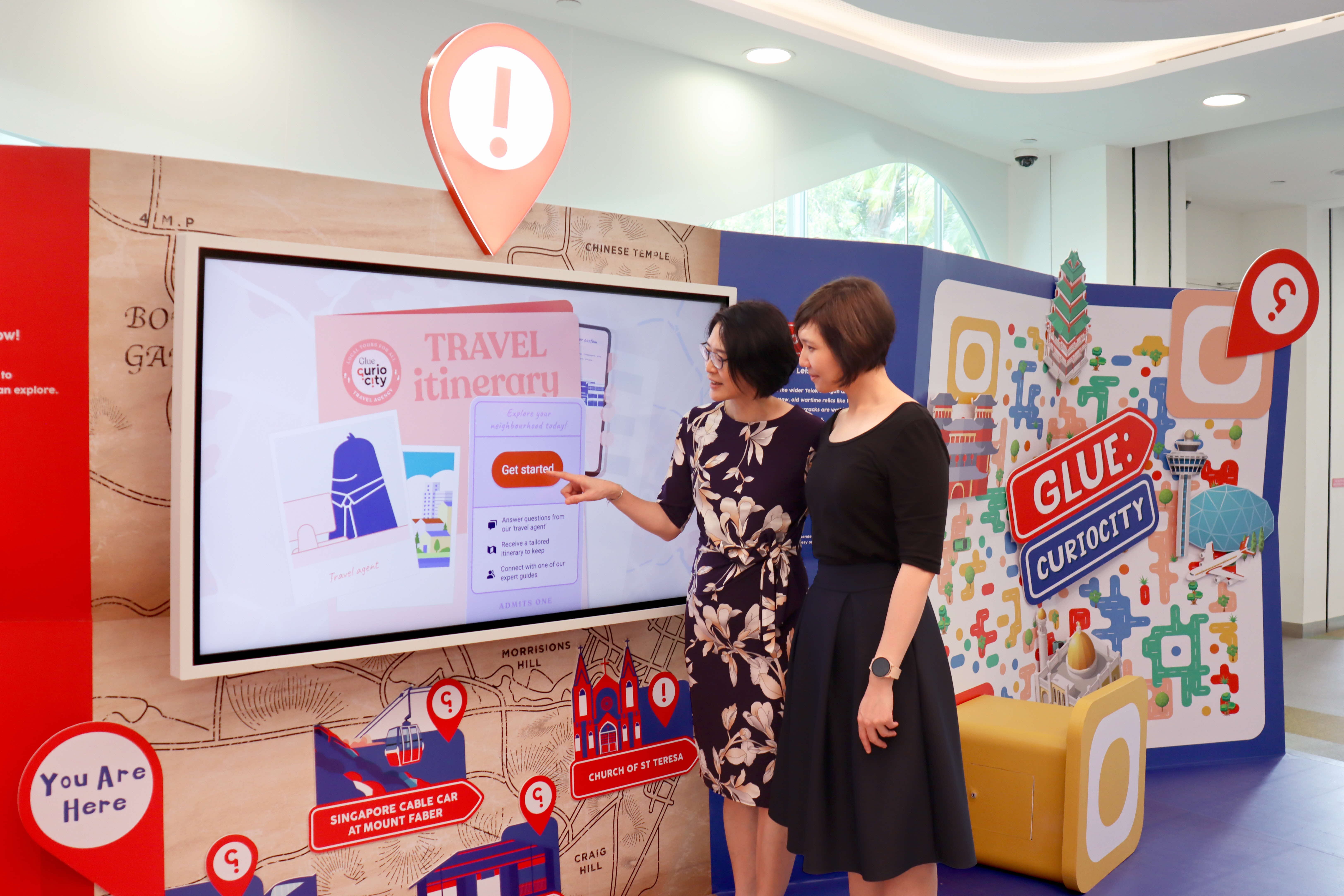 Two people stand in front of a travel itinerary display screen at an interactive exhibition.
