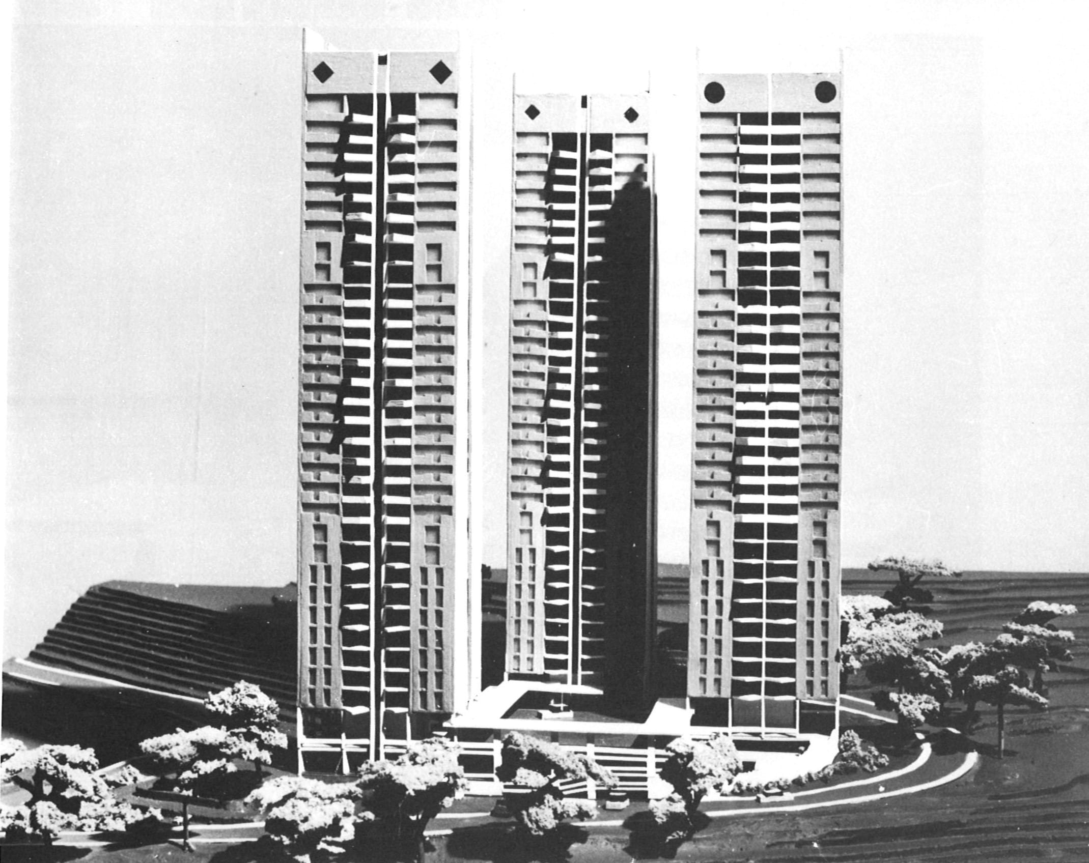 Black and white photo of three identical tall buildings with trees and curving pathway at the base.