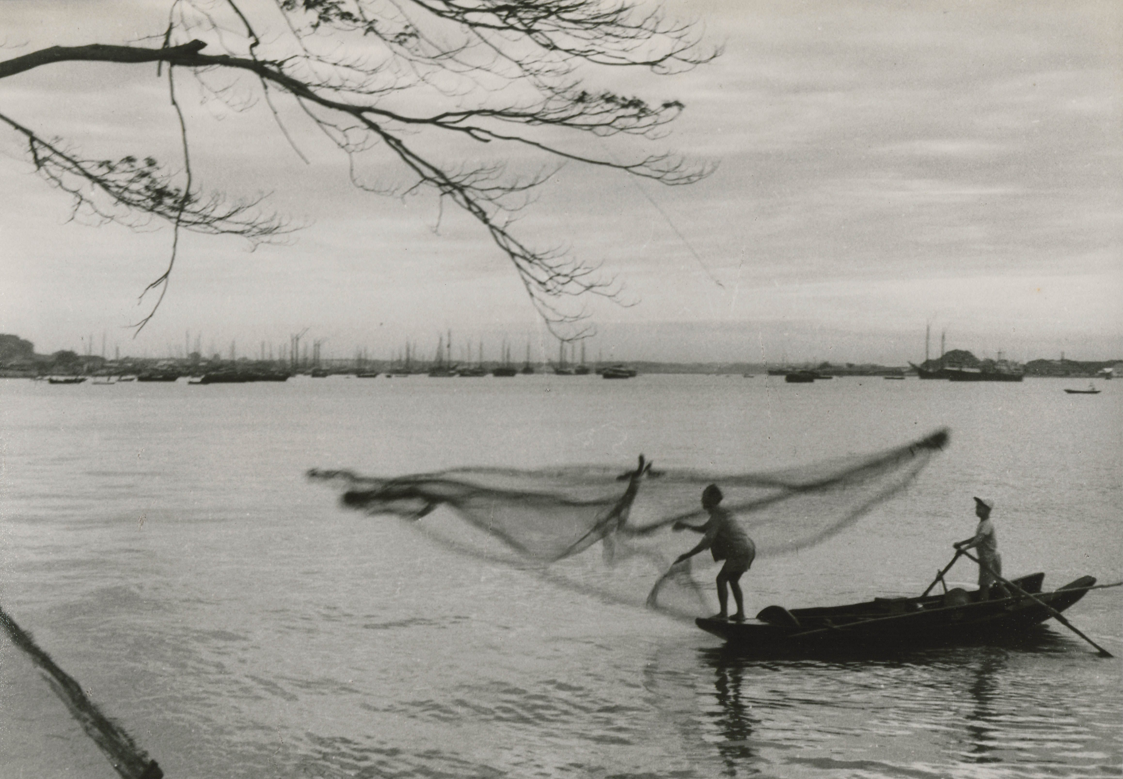 1955 photograph of a man casting a net to catch prawns in Singapore
