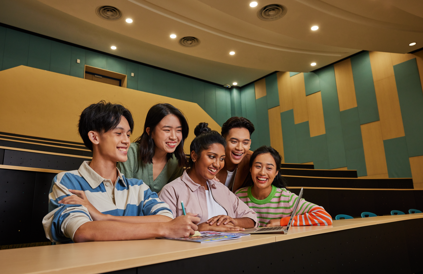 Students seated in a lecture hall using a laptop together, engaged in group study or discussion.