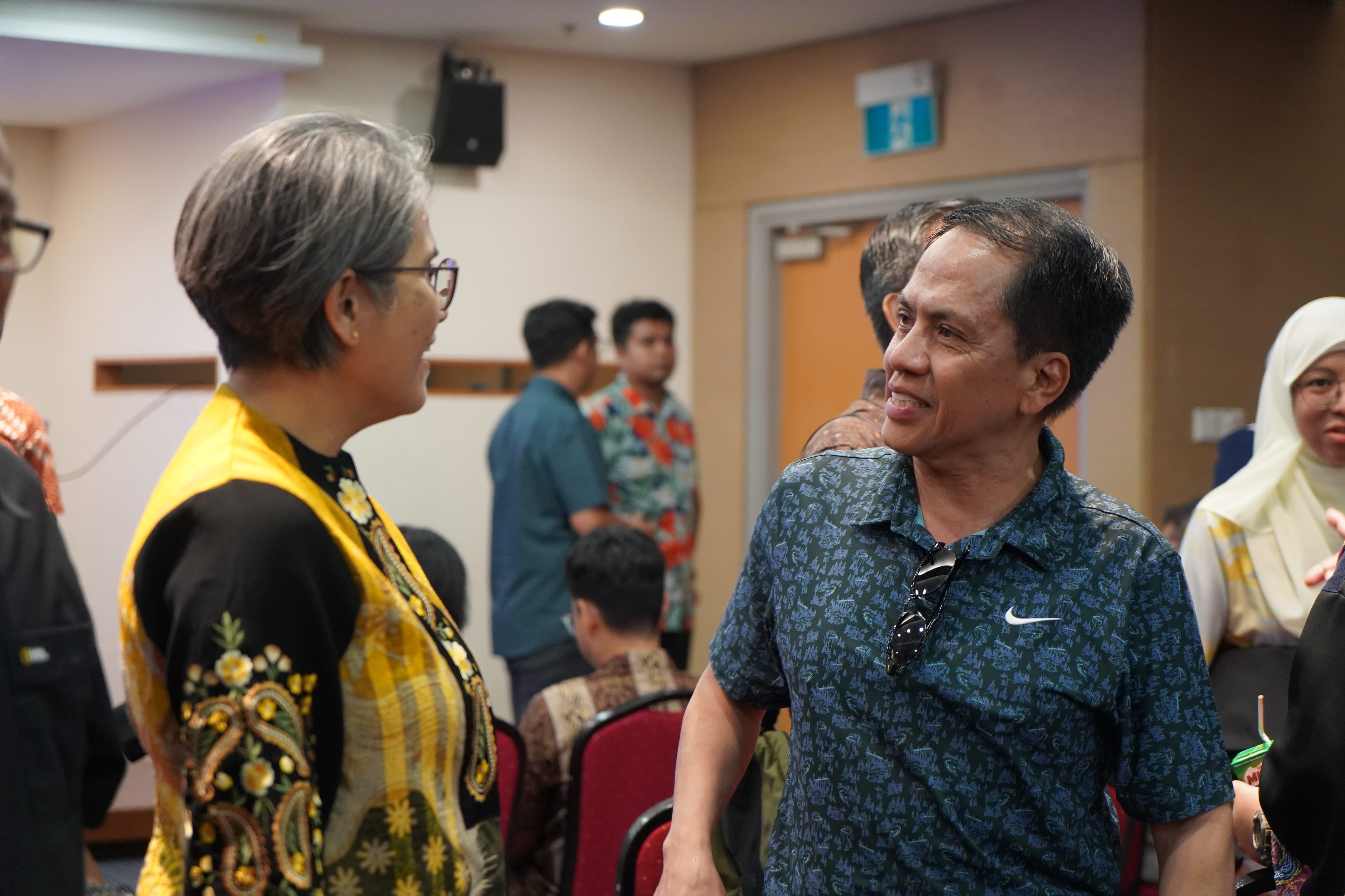 President of LKM speaks with a member after the AGM as attendees mingle in the background.