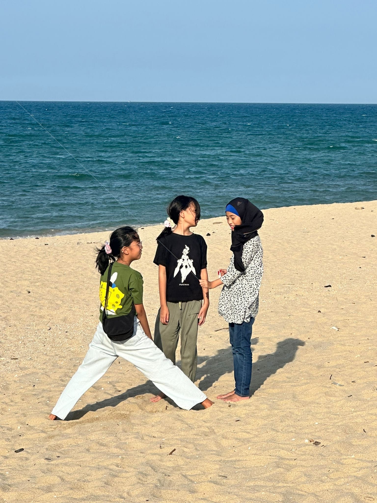 Three children standing barefoot on a sandy beach and chatting beside the shoreline.