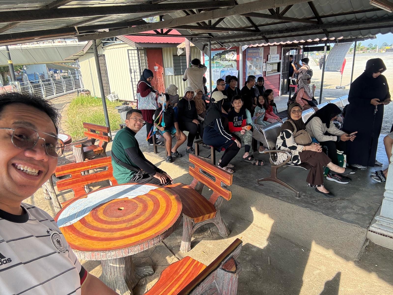 Members and families gathered at a covered waiting area near the beach before a boat activity.