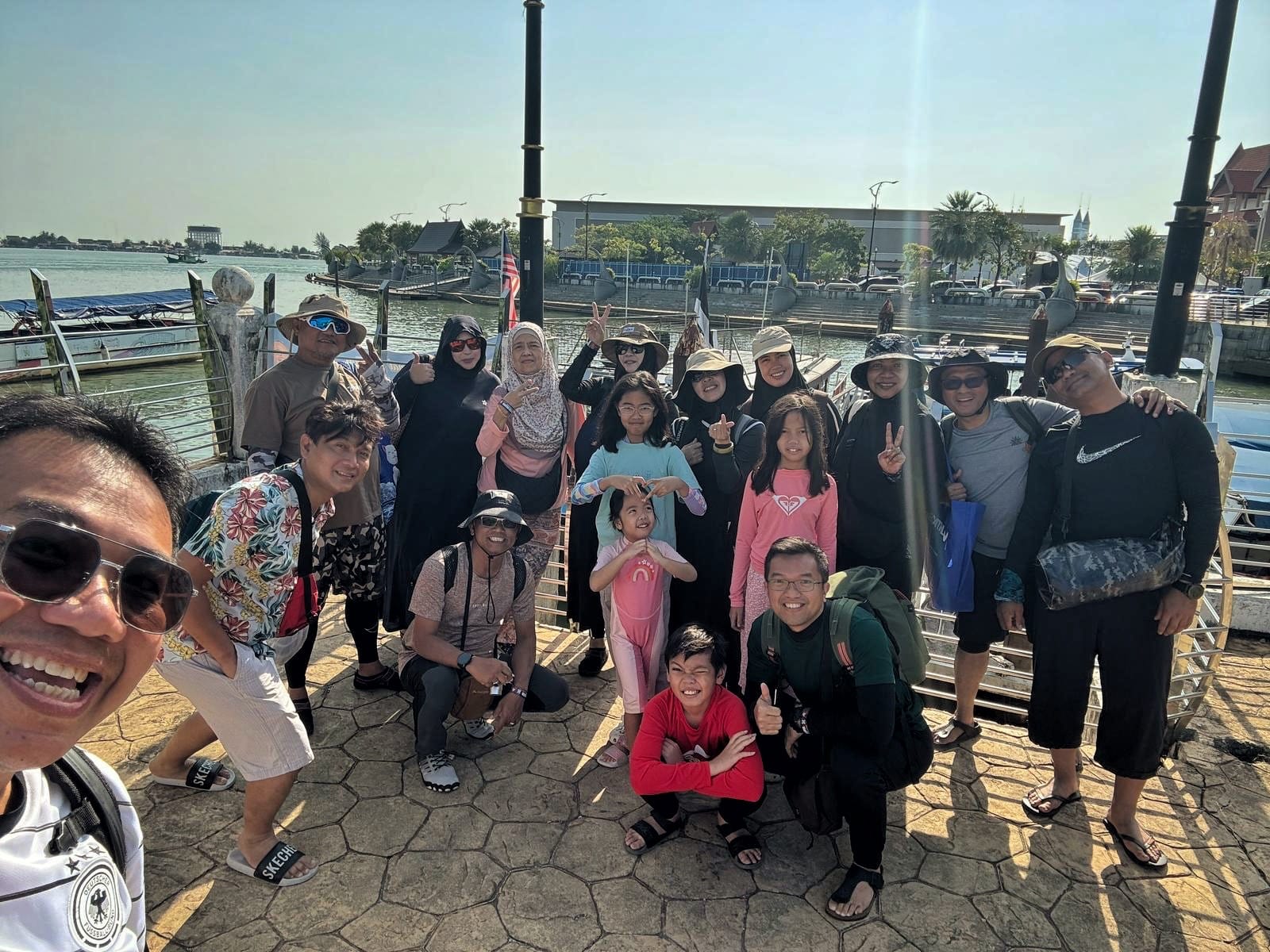 Group photo of LKM members and families posing at a riverside jetty before boarding a boat excursion.