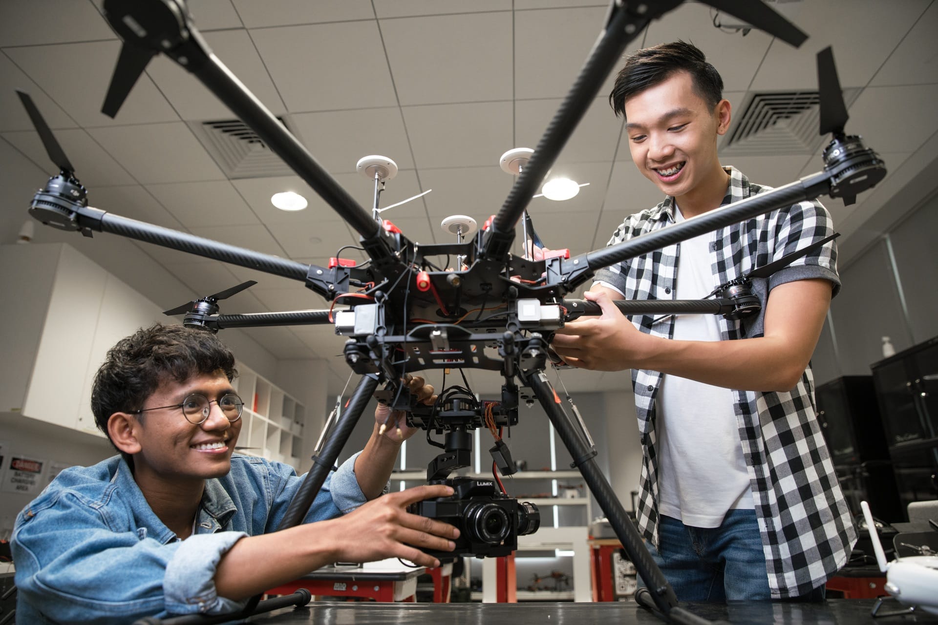 Two students examining a large drone in a modern classroom