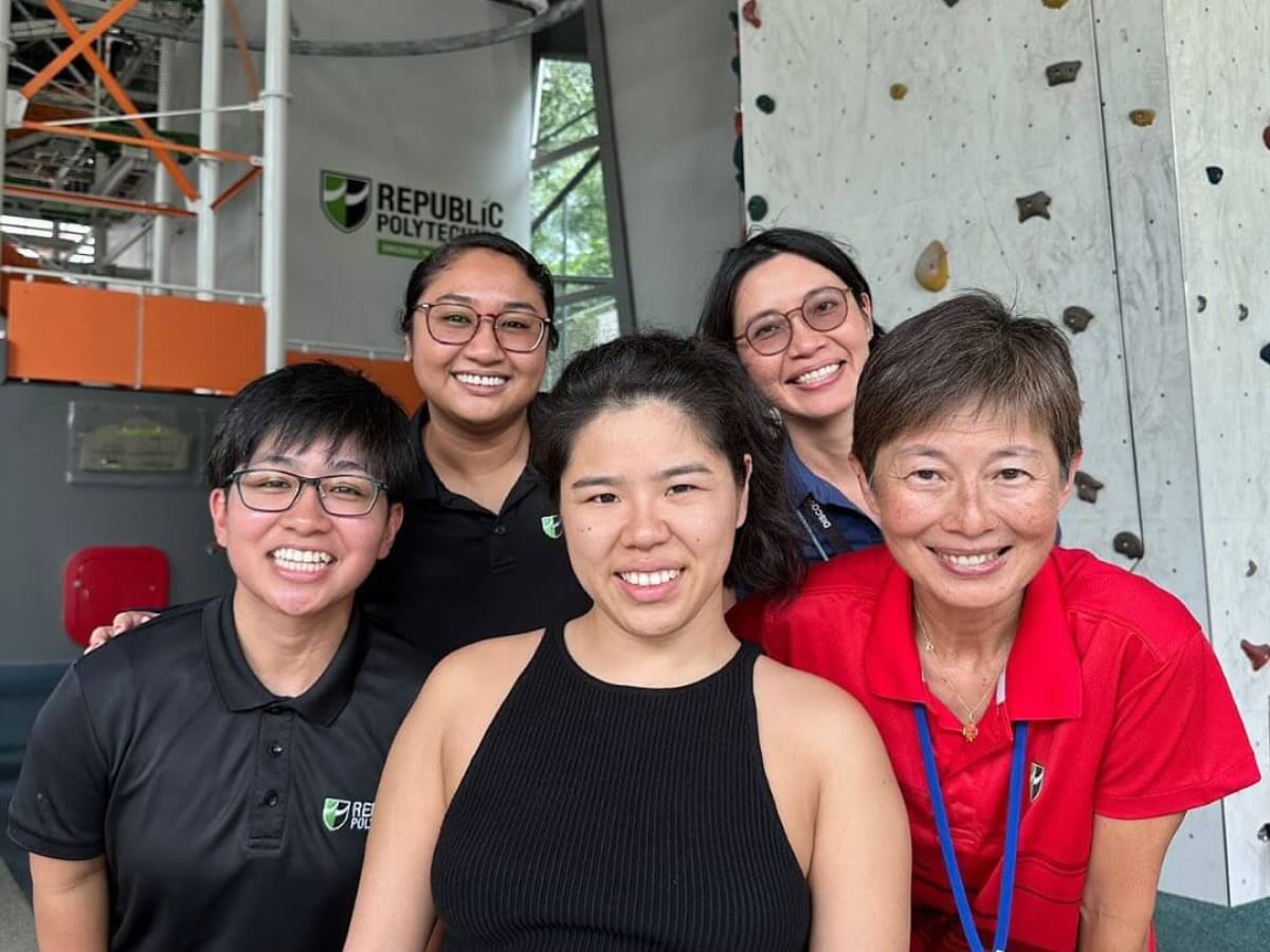 Five smiling women pose at Republic Polytechnic, by an indoor climbing wall.