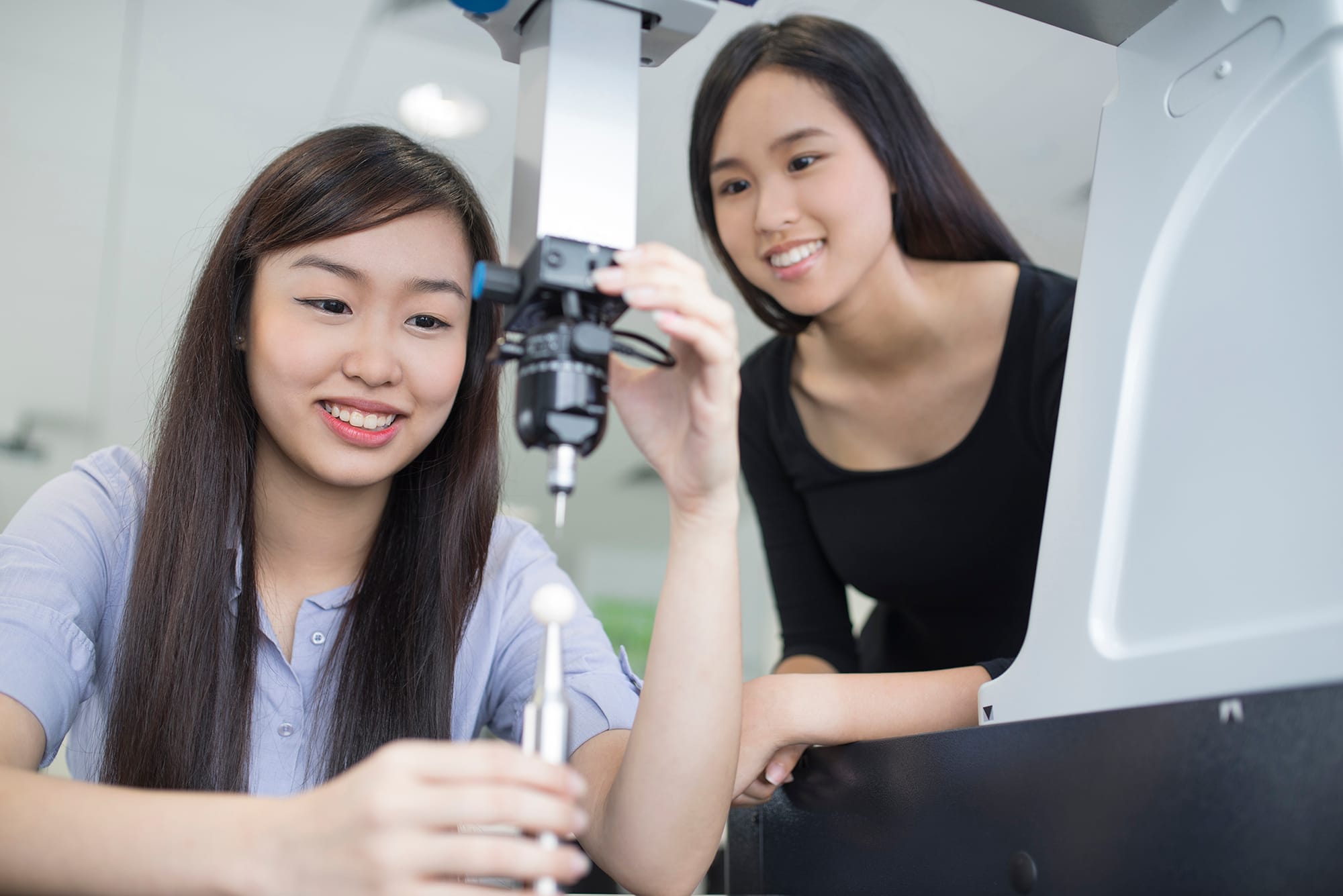 Two young women operate a 3D printer in a bright lab