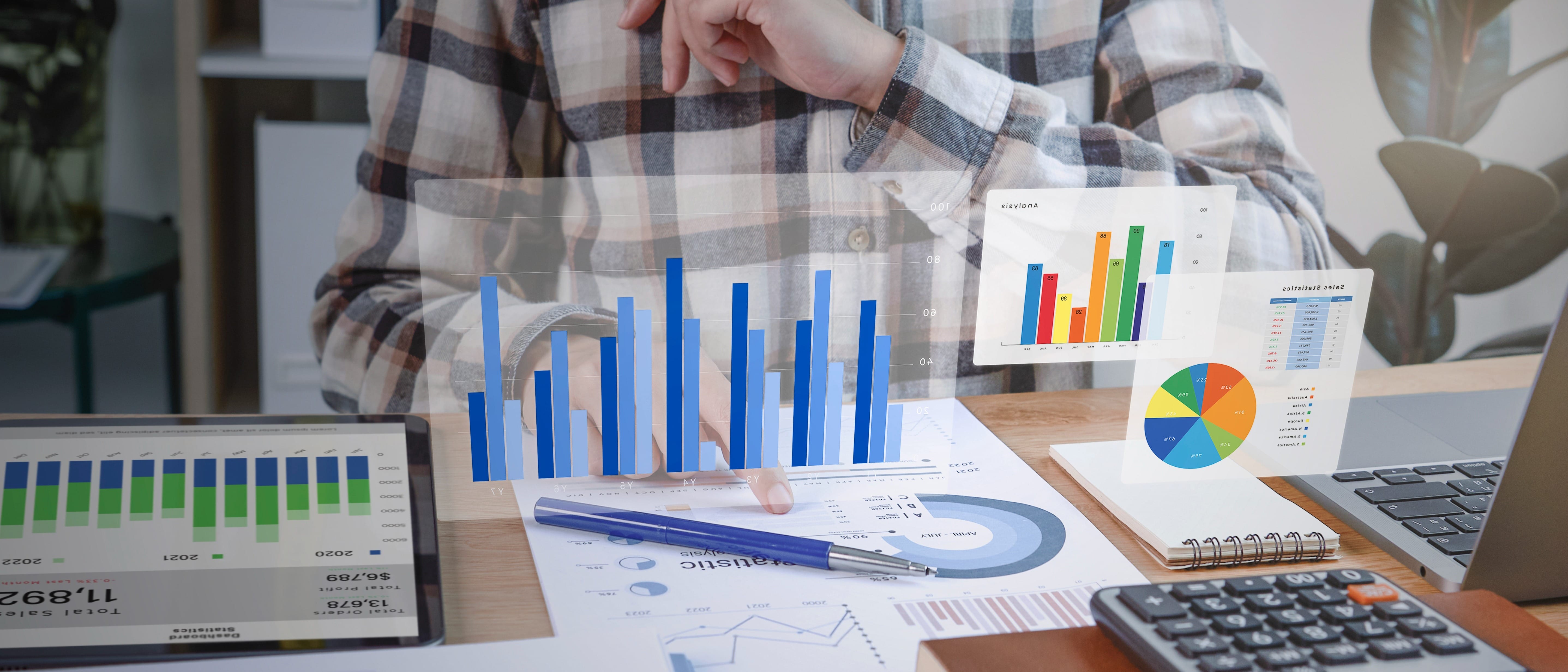 A person in a plaid shirt analyzes data with colorful bar and pie charts on papers and digital devices.