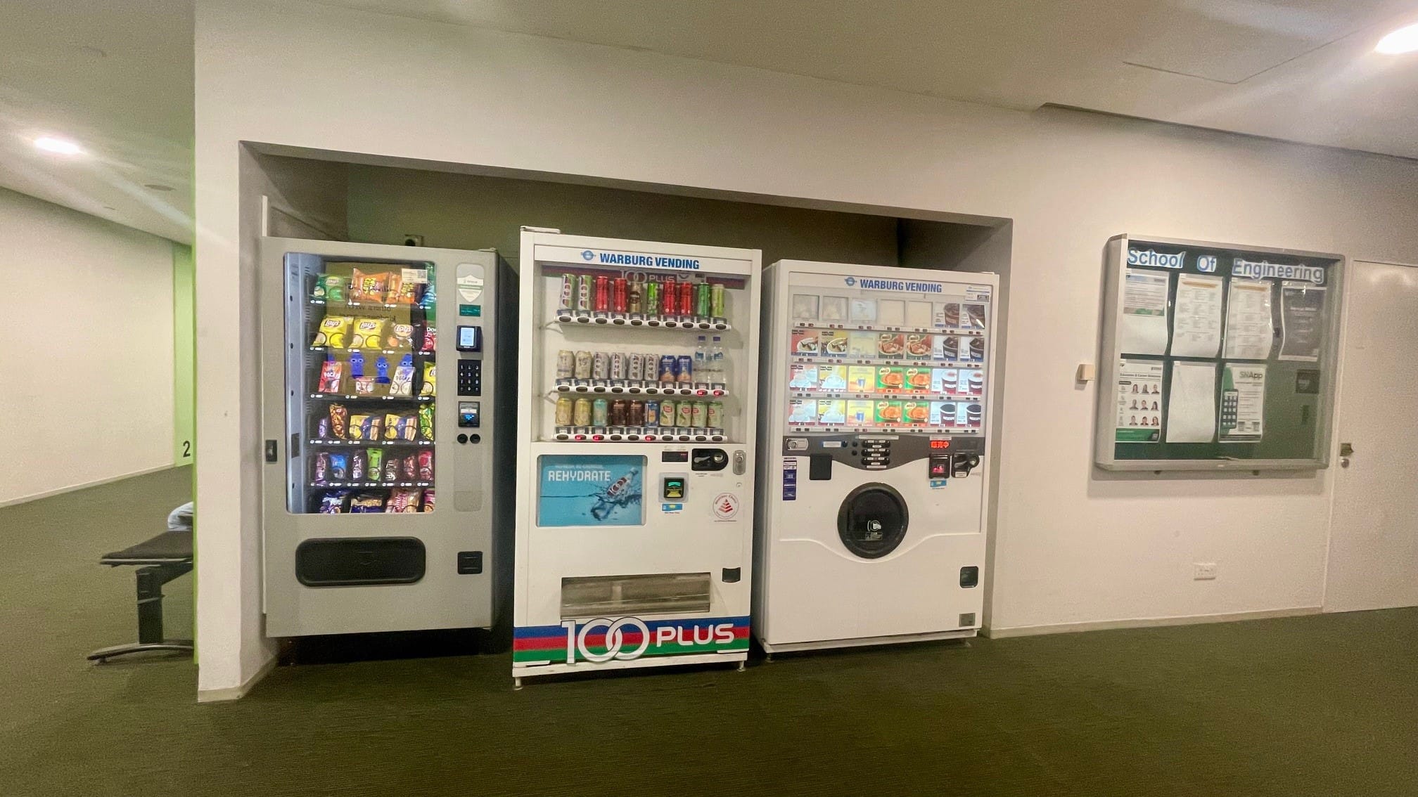 Three vending machines offering snacks and drinks located near a student services area.