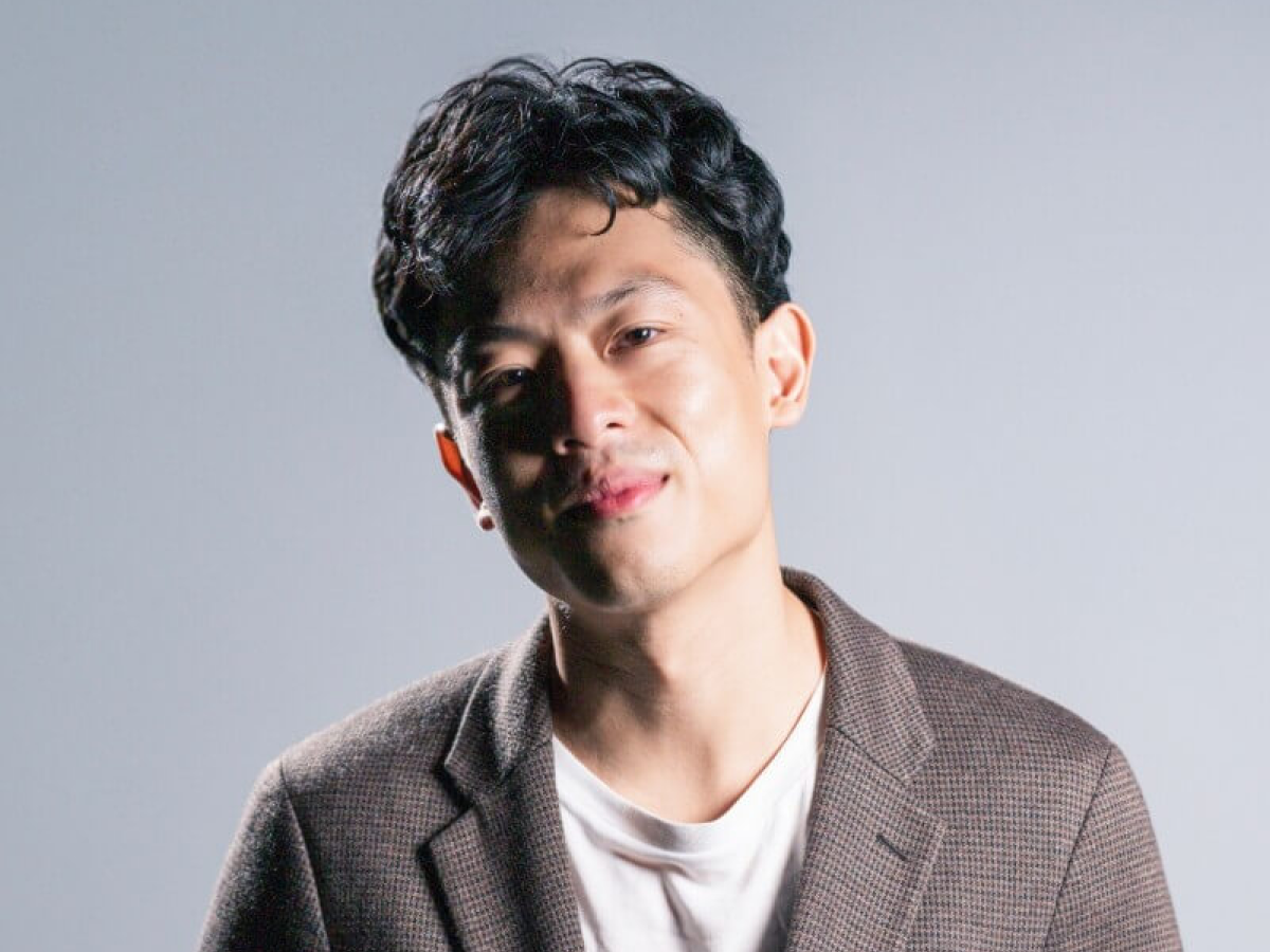 Man in blazer and white shirt on gray background.