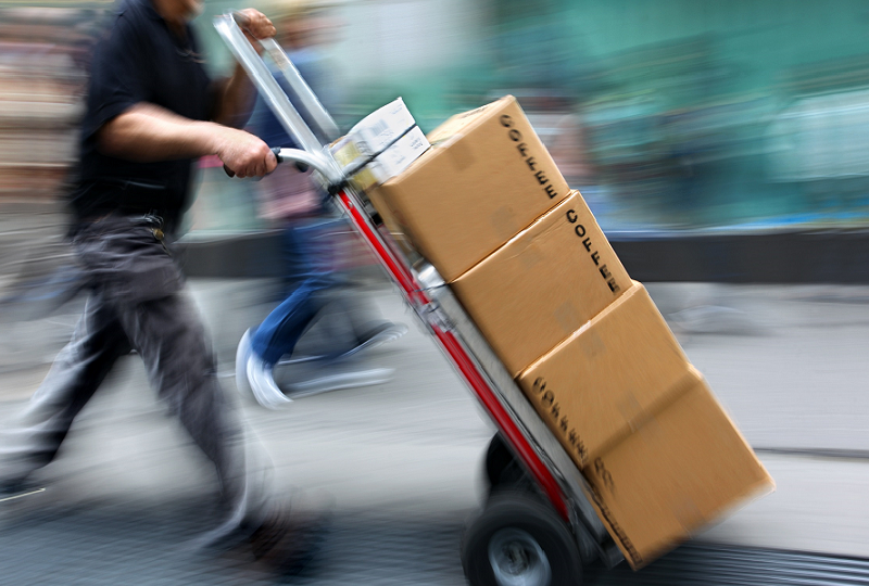 Worker pushing a hand truck loaded with cardboard boxes, captured in motion.