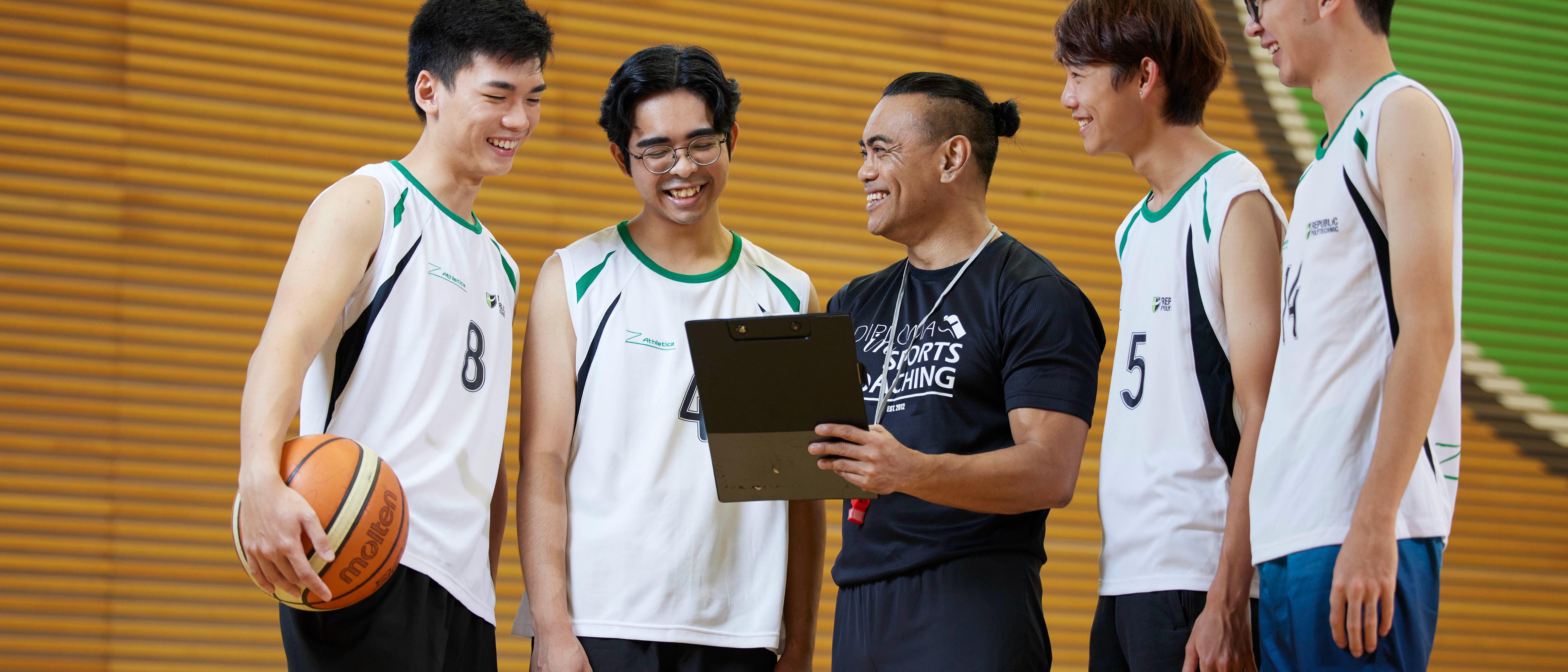 Sports coach reviewing strategy with basketball players during a training session, highlighting coaching education and athlete development.