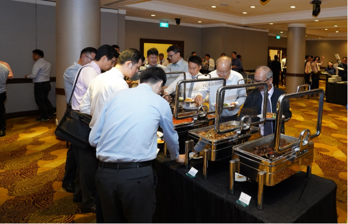 People in business attire serving themselves food from buffet chafing dishes at a formal event.