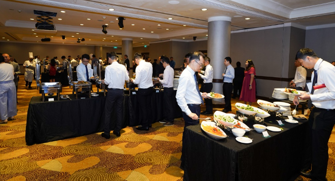 People in formal attire serving themselves at a buffet spread in a large banquet hall.