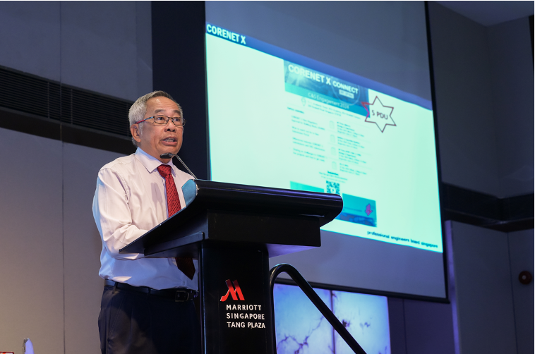 Man in white shirt and red tie speaking at a Marriott Singapore Tang Plaza podium with a CORENET X presentation behind him.