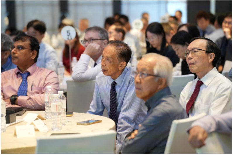 A crowded conference room with many seated attendees in formal attire, one person holding up a bidding paddle.