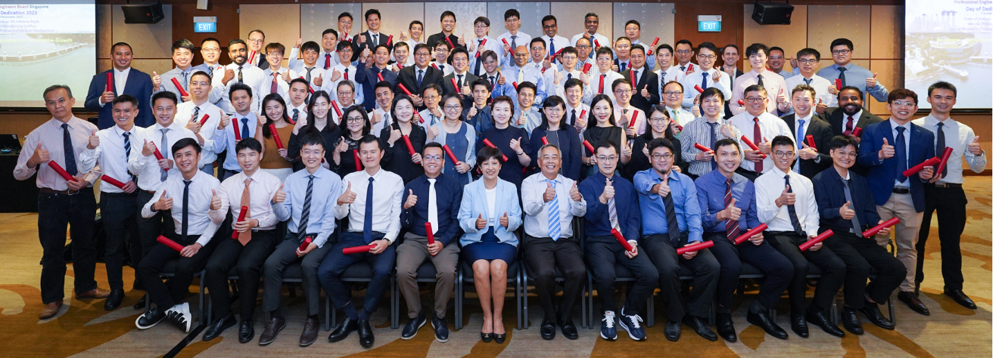Large group of formally dressed people posing with red certificate scrolls and thumbs up at a 2023 dedication ceremony.