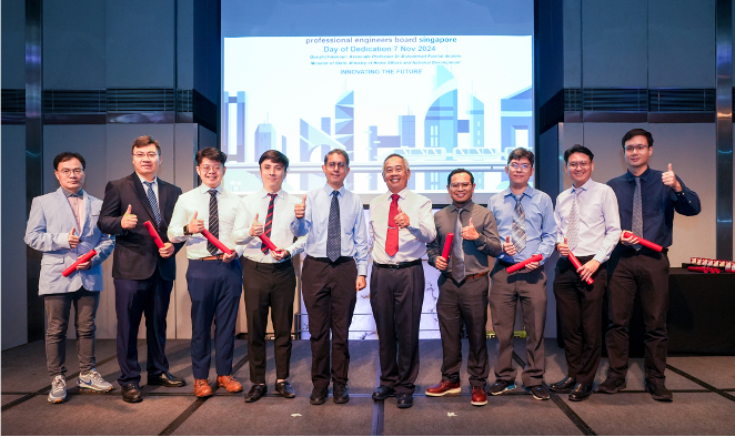 Nine men in formal attire pose with thumbs up holding red scrolls at a Professional Engineers Board Singapore event.
