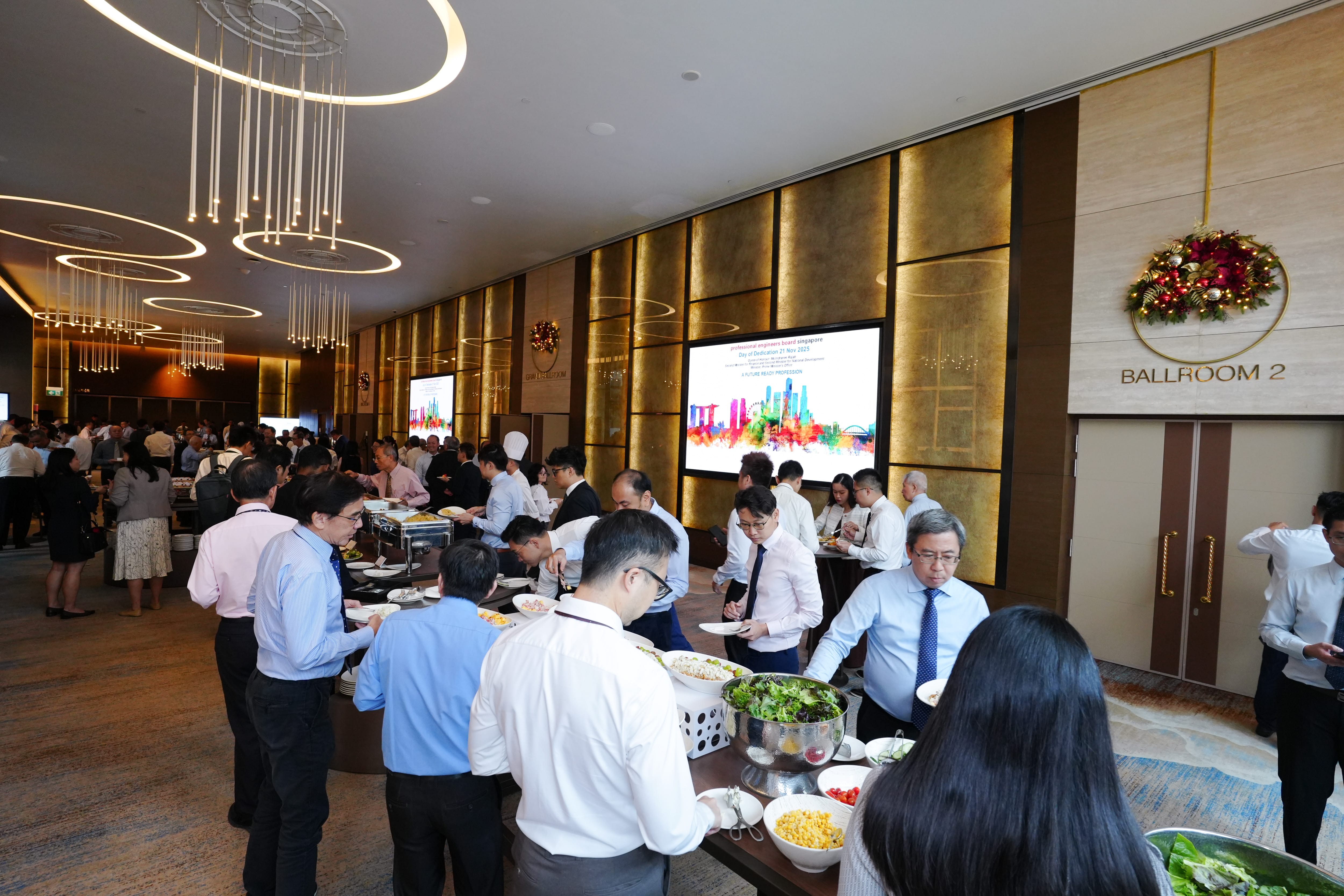 People in business attire serving themselves at a buffet outside Ballroom 2 in a modern hotel venue.
