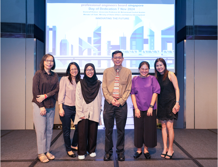 Six people posing together in front of a projected slide for Professional Engineers Board Singapore Day of Dedication 2024.