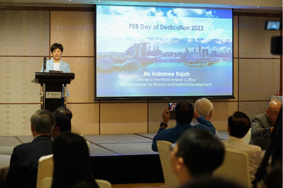 Ms Indranee Rajah speaks at a podium during PEB Day of Dedication 2023, with a projected slide behind her.