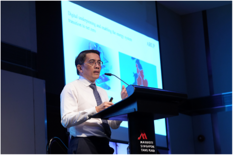 A man in a white shirt and tie speaks at a podium at Marriott Singapore Tang Plaza with a blue presentation slide behind him.