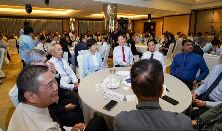 A large group of formally dressed people seated at round tables in a banquet hall during a conference event.