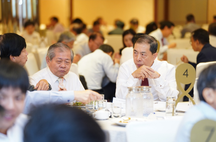 Two older men in white shirts sit at a banquet table numbered 4, surrounded by other seated guests.