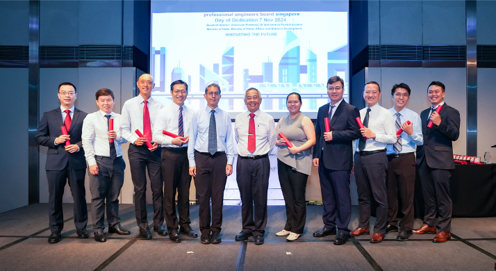Ten people stand in a row holding red scrolls at a Professional Engineers Board Singapore ceremony.