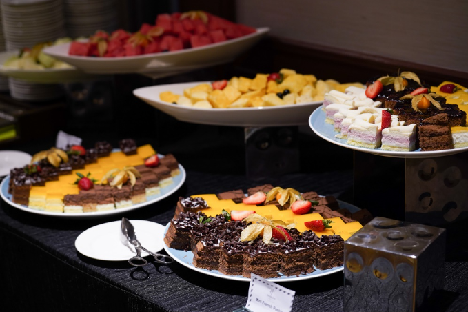 Buffet table with chocolate cake slices topped with strawberries, fruit platters, and assorted bite-sized desserts.