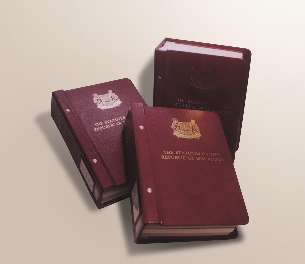 Three dark red hardcover volumes titled "The Statutes of the Republic of Singapore" with gold embossed text and crest.