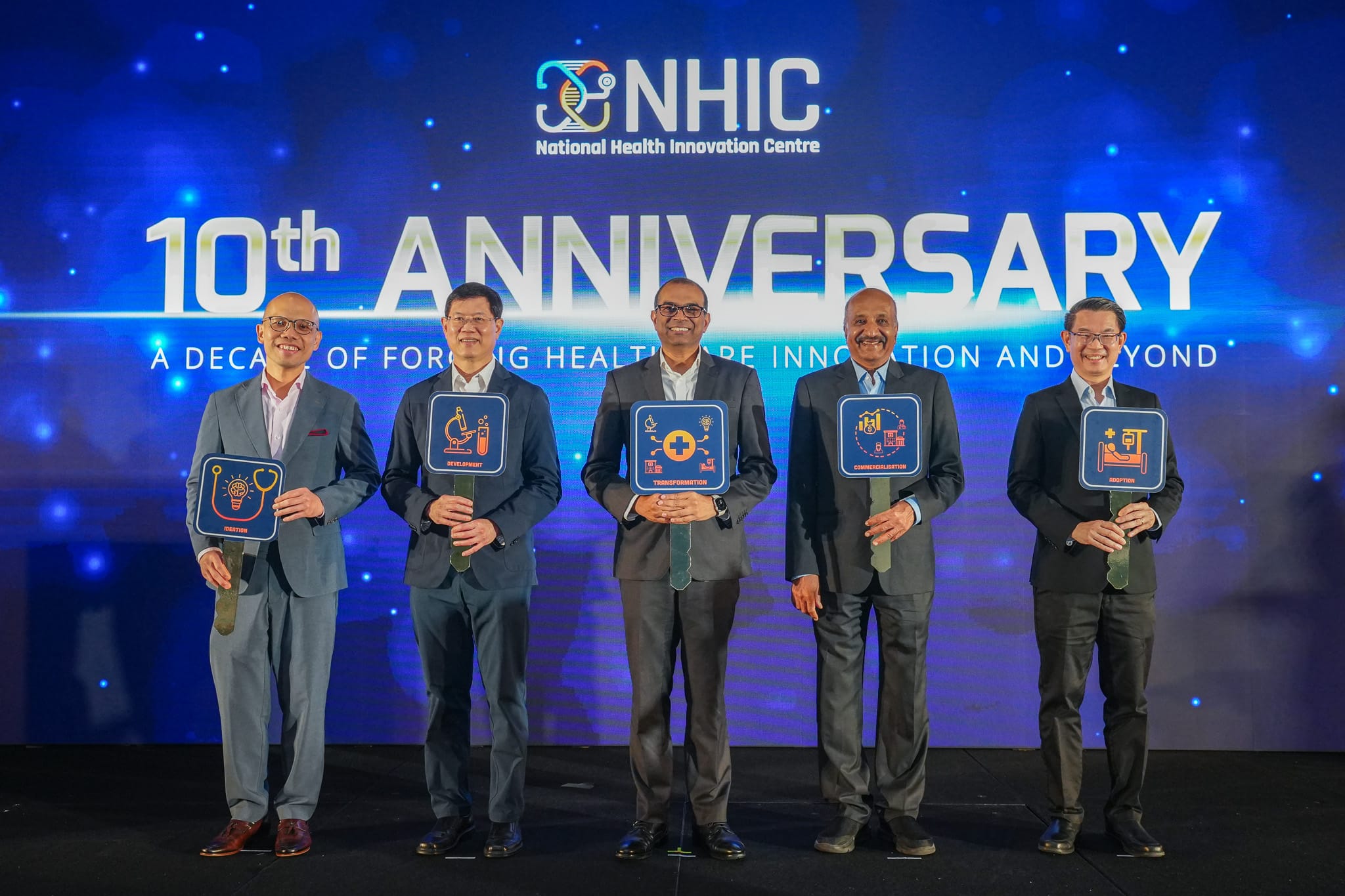 Five men in suits hold icon plaques on stage at the NHIC 10th Anniversary event celebrating healthcare innovation.